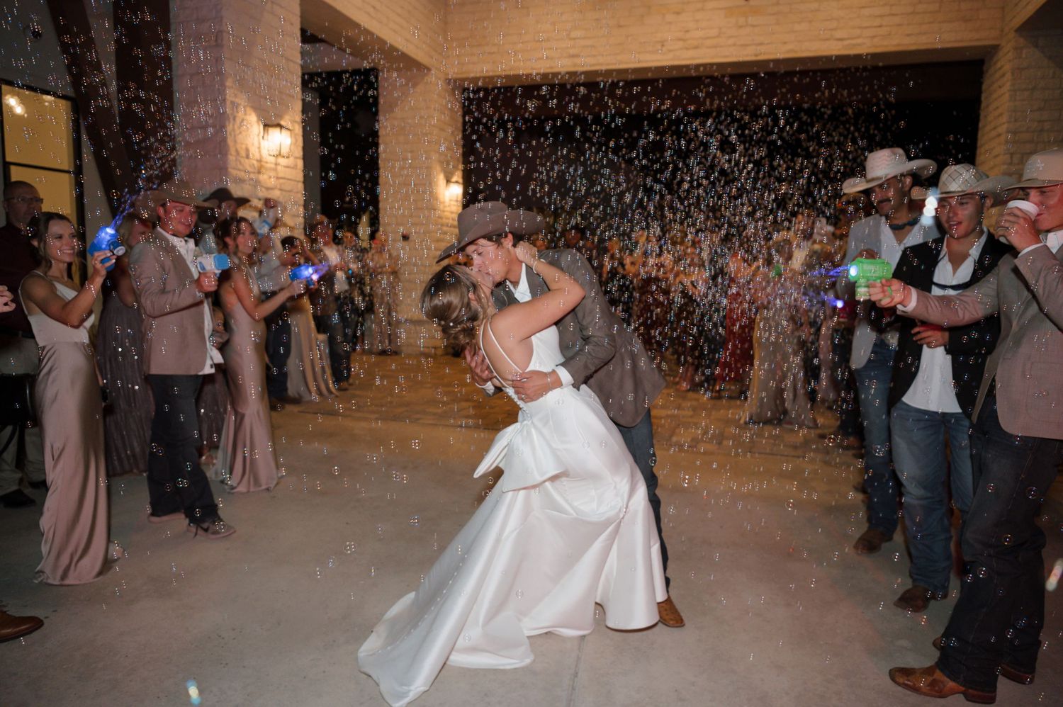 A couple exits their wedding in Texas with their guests blowing bubbles with bubble guns photographed by Alyssa Denson Photography.
