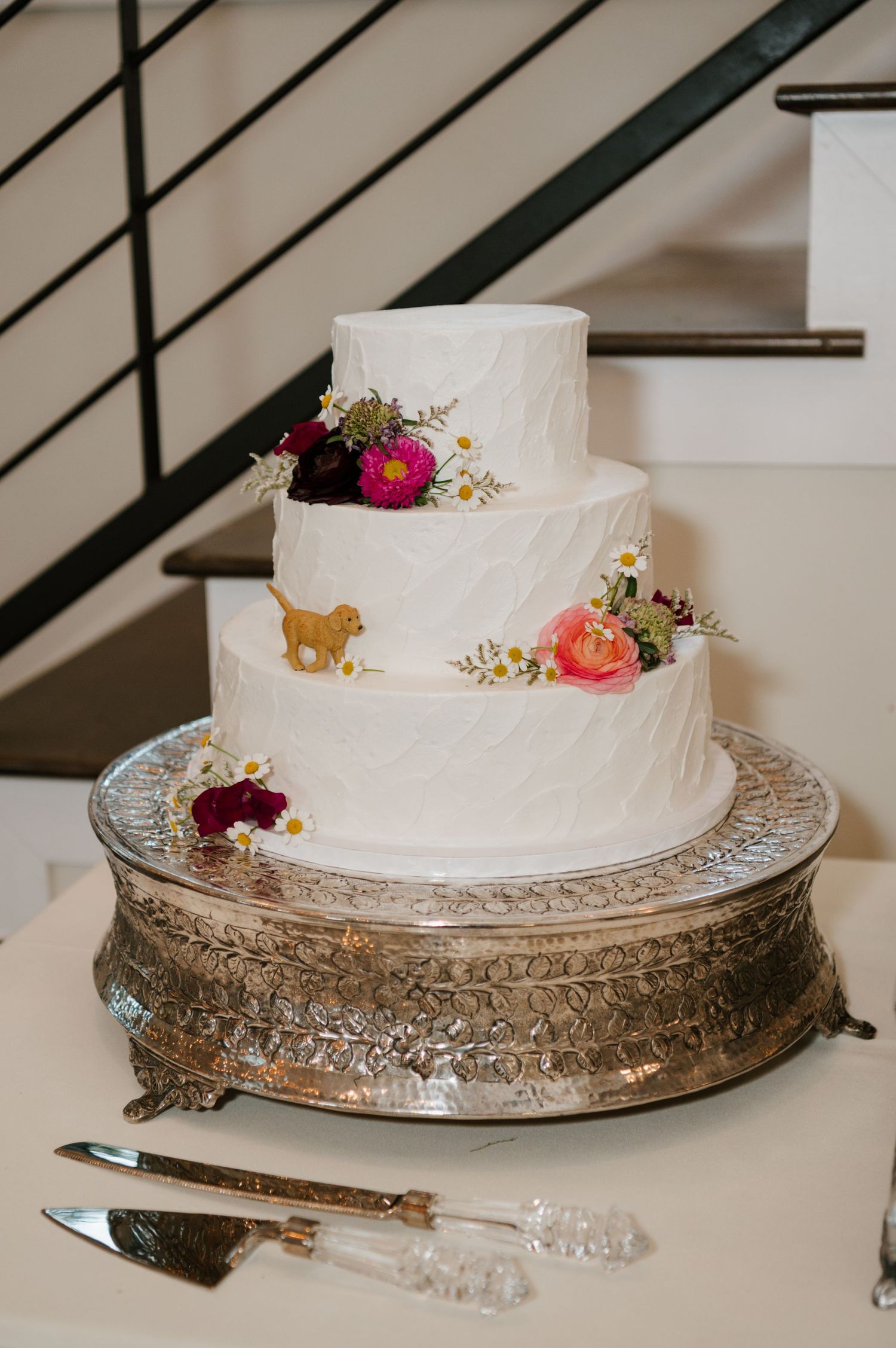 Simple white wedding cake displayed on an ornate silver platter with small floral decorations.