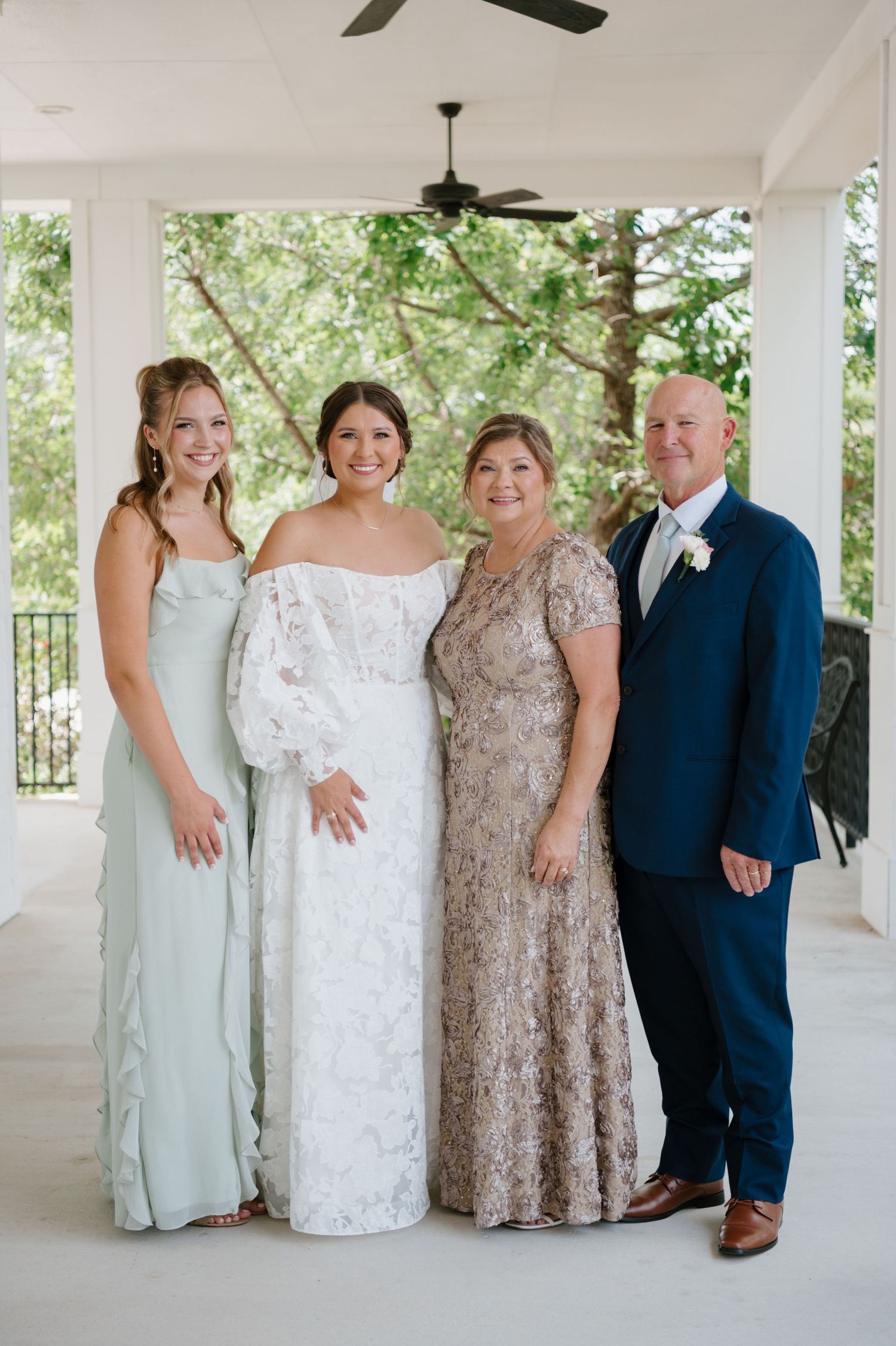 Wedding party poses on an elegant white porch with lush greenery backdrop wearing formal attire.