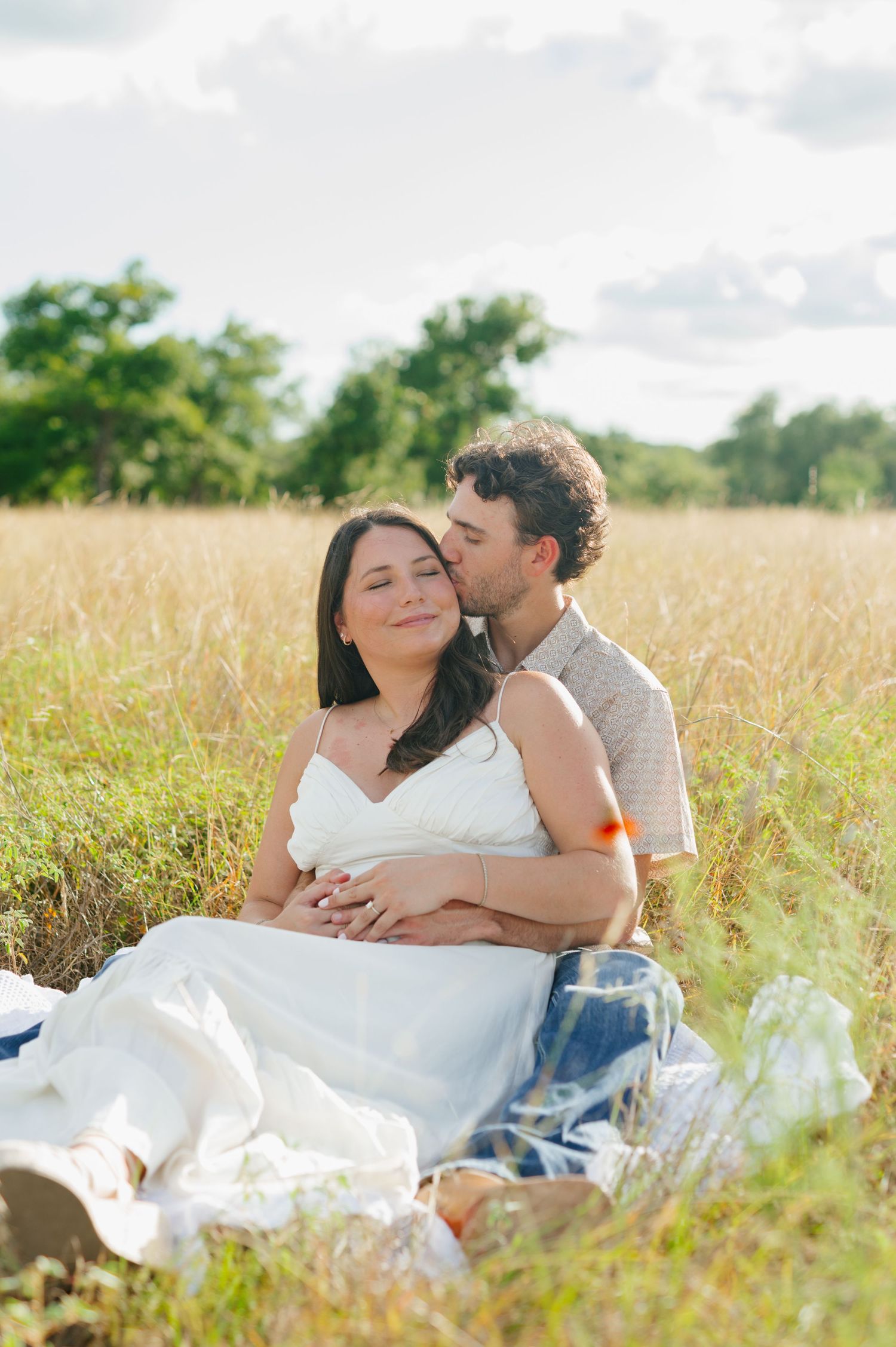 A couple sharing intimate moments while lounging in a sun-drenched field of tall grass.