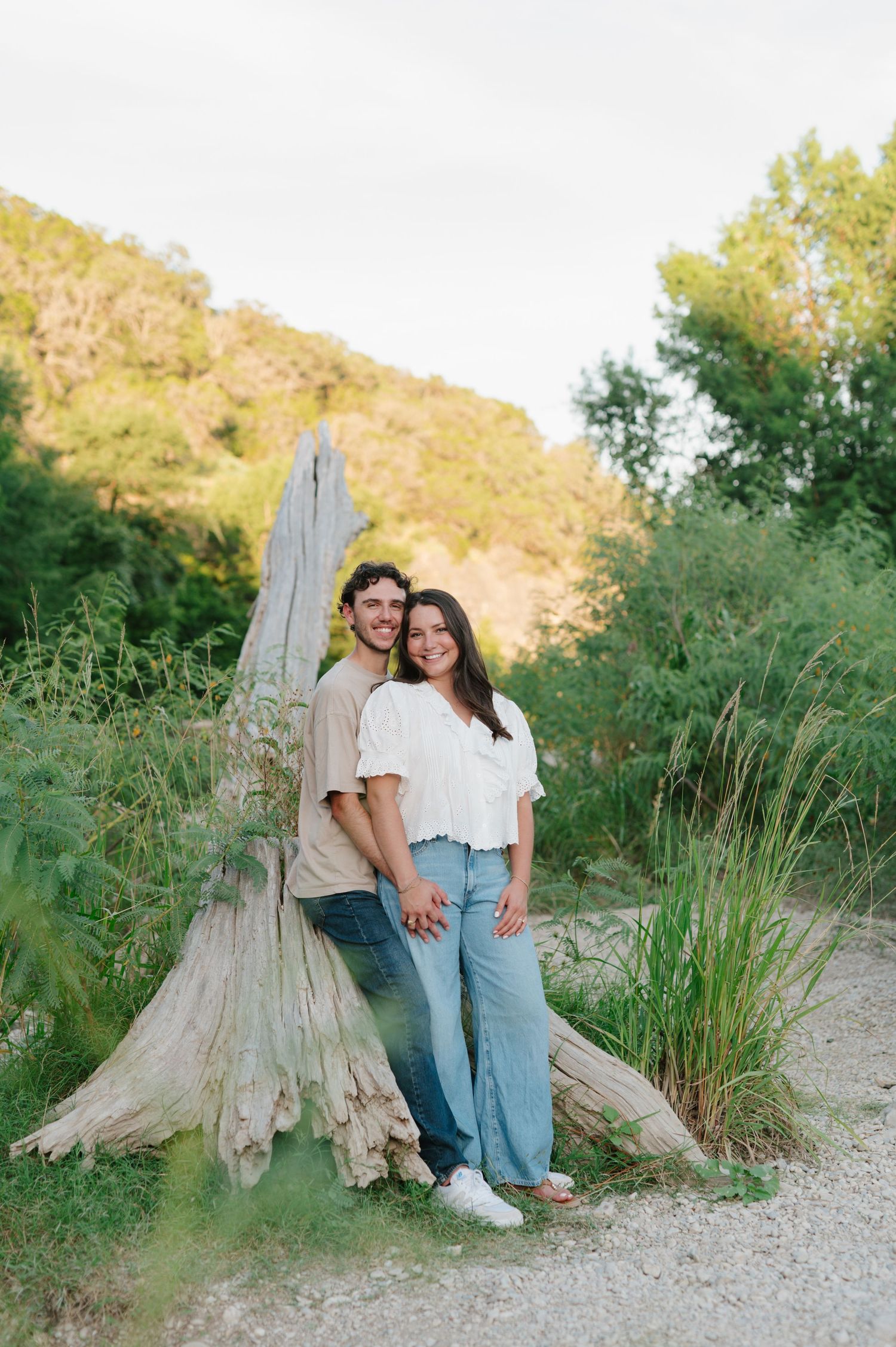 Casual couple's portrait by weathered tree stump in natural outdoor setting.