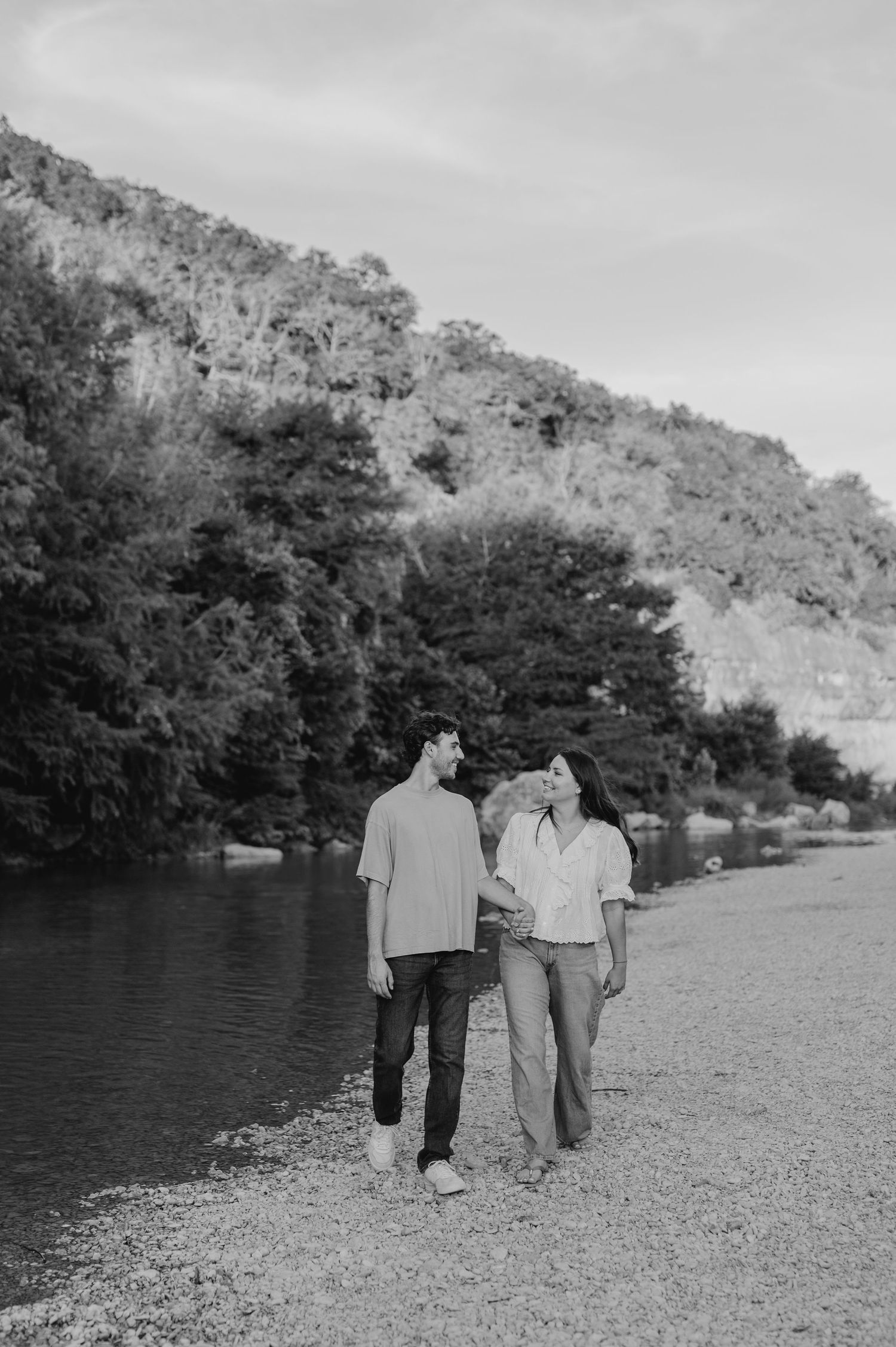 A couple walking along a riverbank in black and white photography.