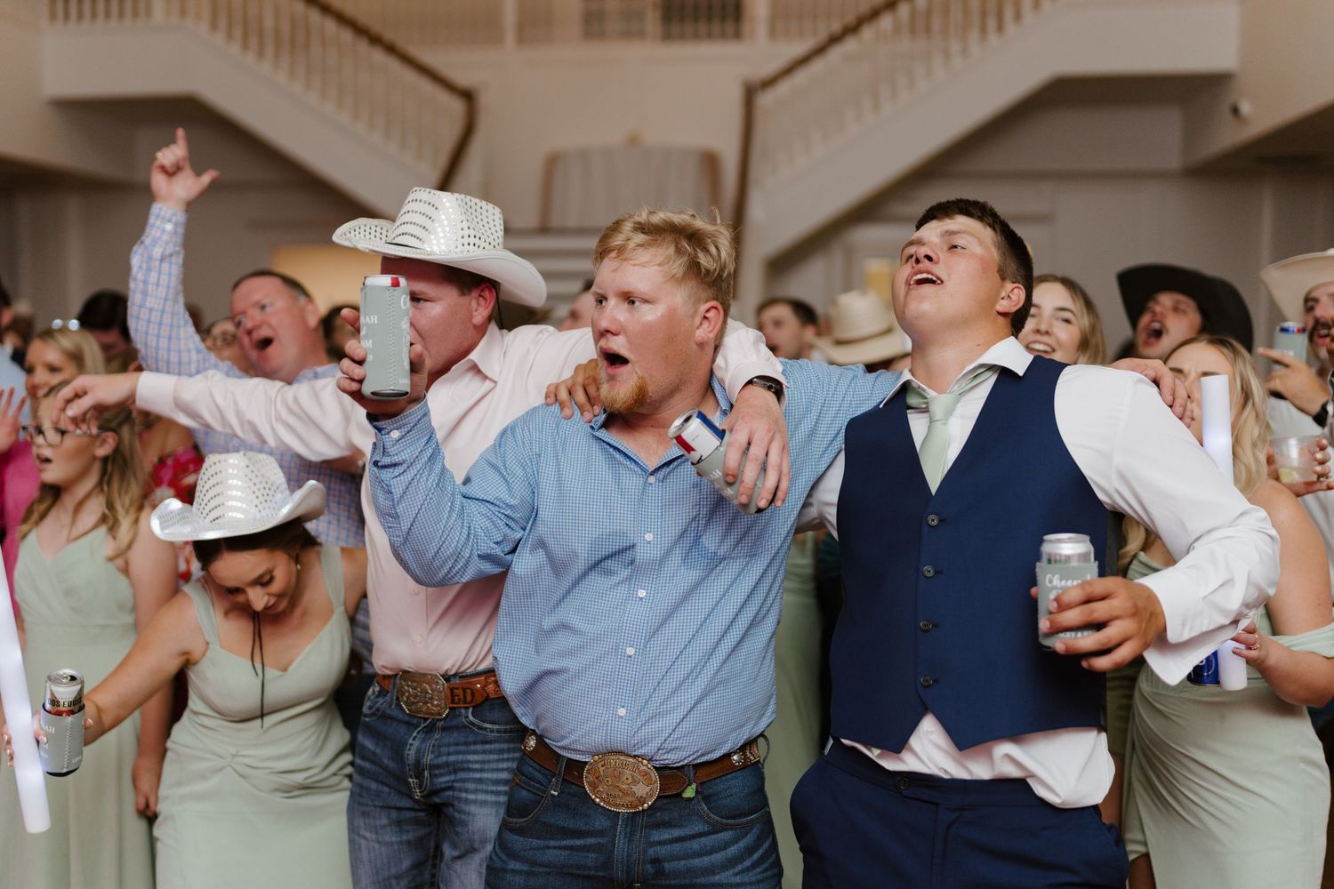Wedding guests dance and celebrate enthusiastically at indoor reception venue.