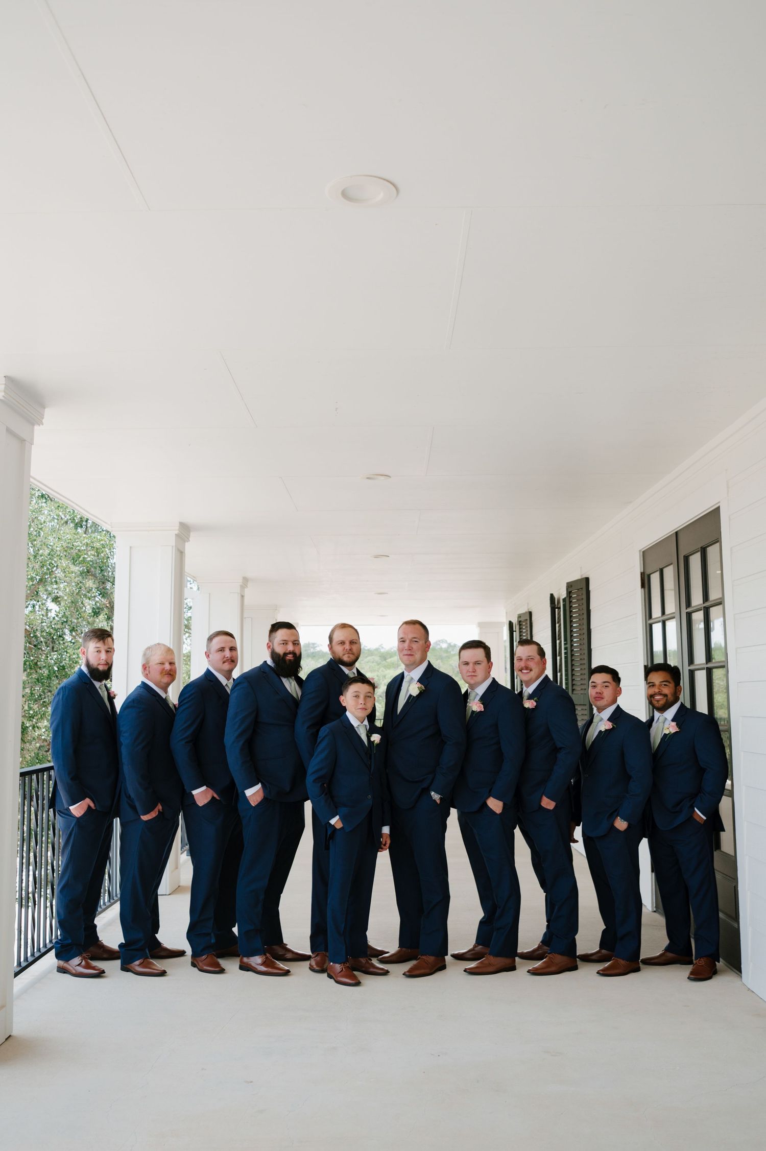 Groomsmen lined up in navy suits along a classic white porch for wedding photos.