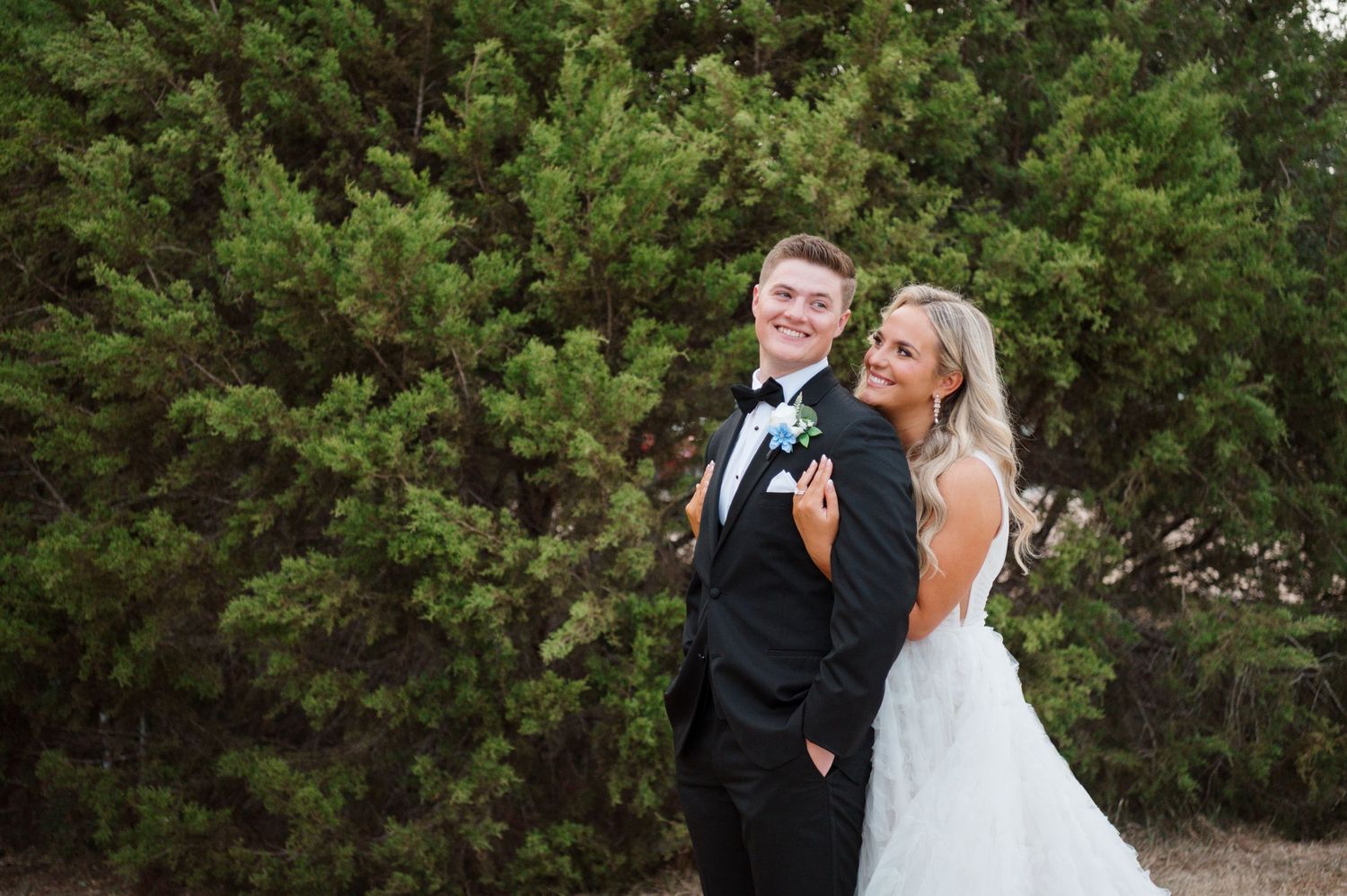 A bride and groom posing together in a wooded outdoor setting.