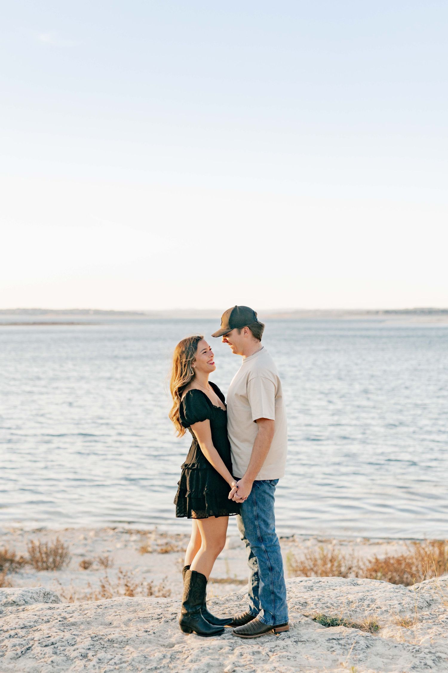 A loving couple stands together on a coastal shoreline during a beautiful sunny day.
