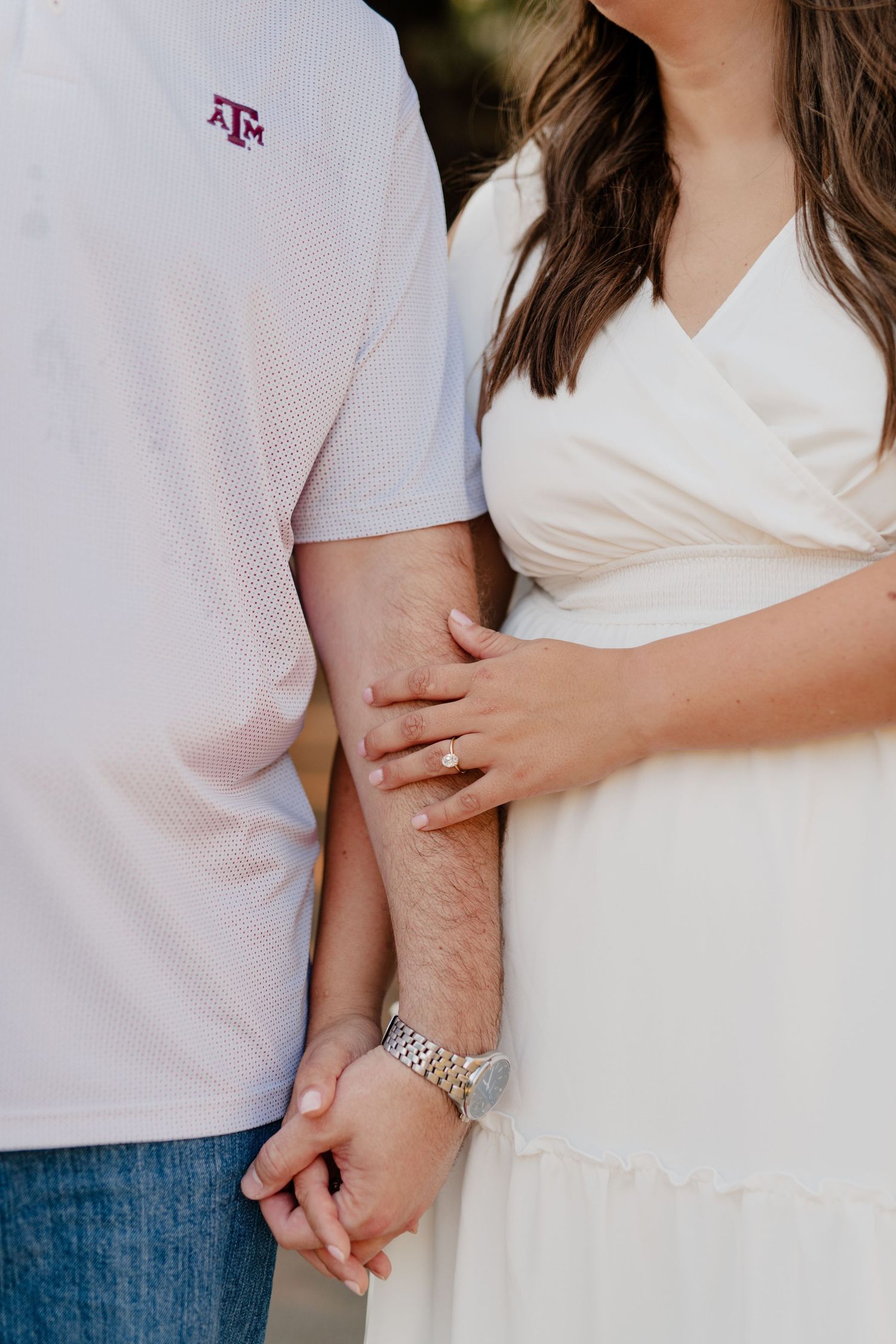 Close-up detail of Texas A&M logo on white polo shirt and hands holding.