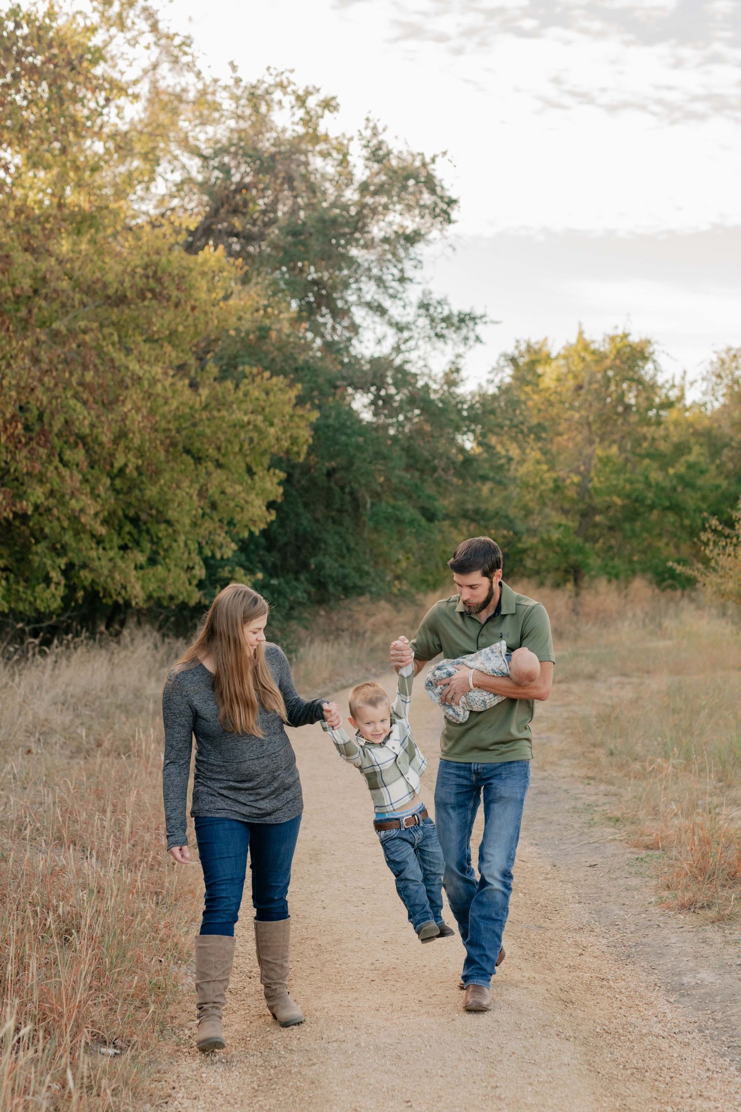 Parents swinging child between them while walking on a nature trail.