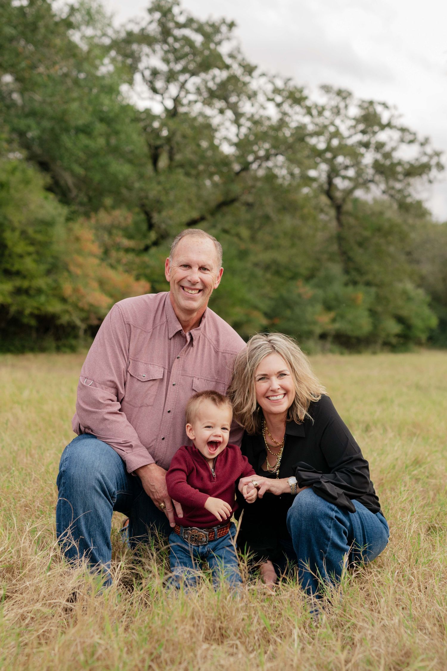 A family of three poses together in a grassy field during an autumn photo session.