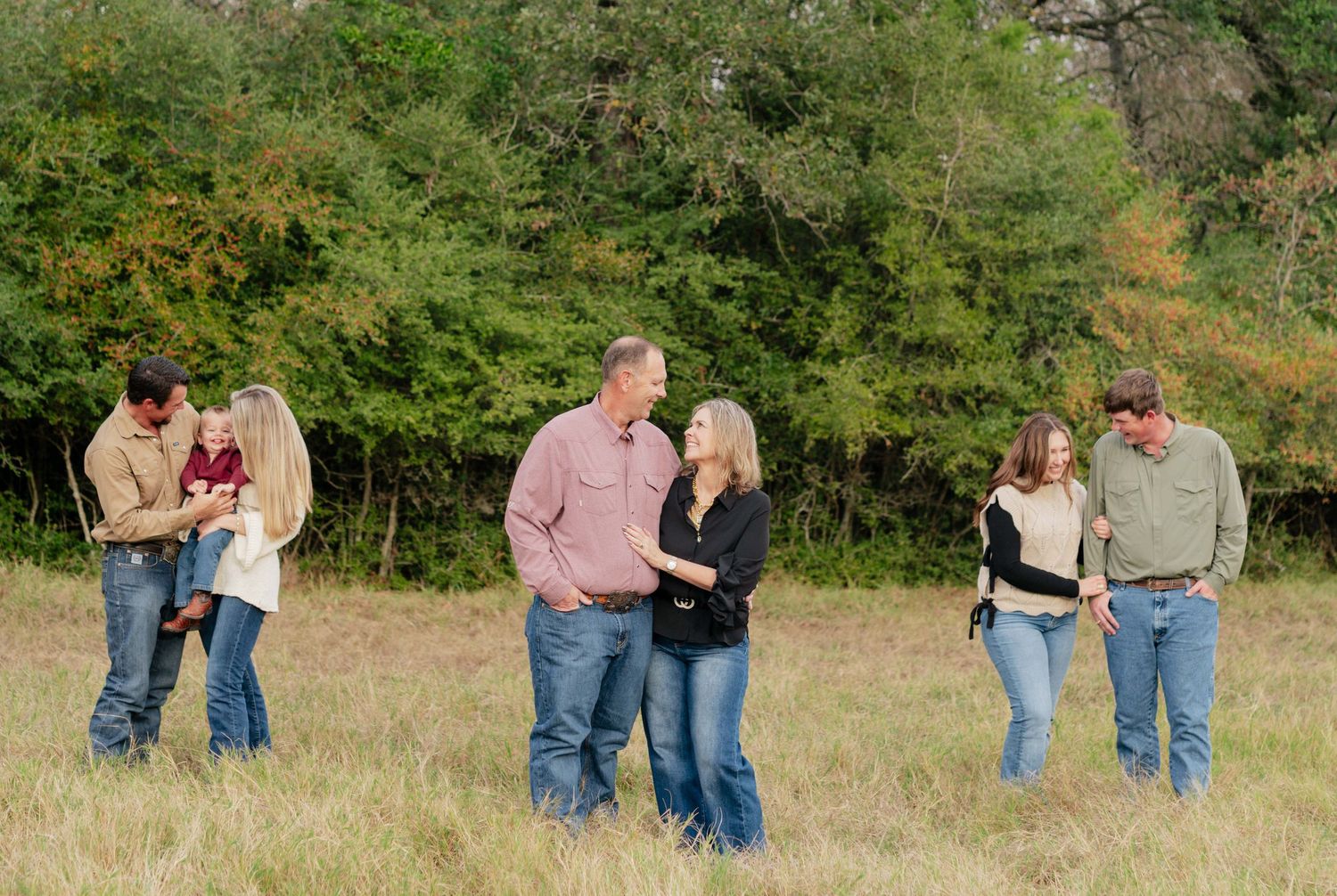 Three couples stand in a grassy field with trees in the background on an autumn day.