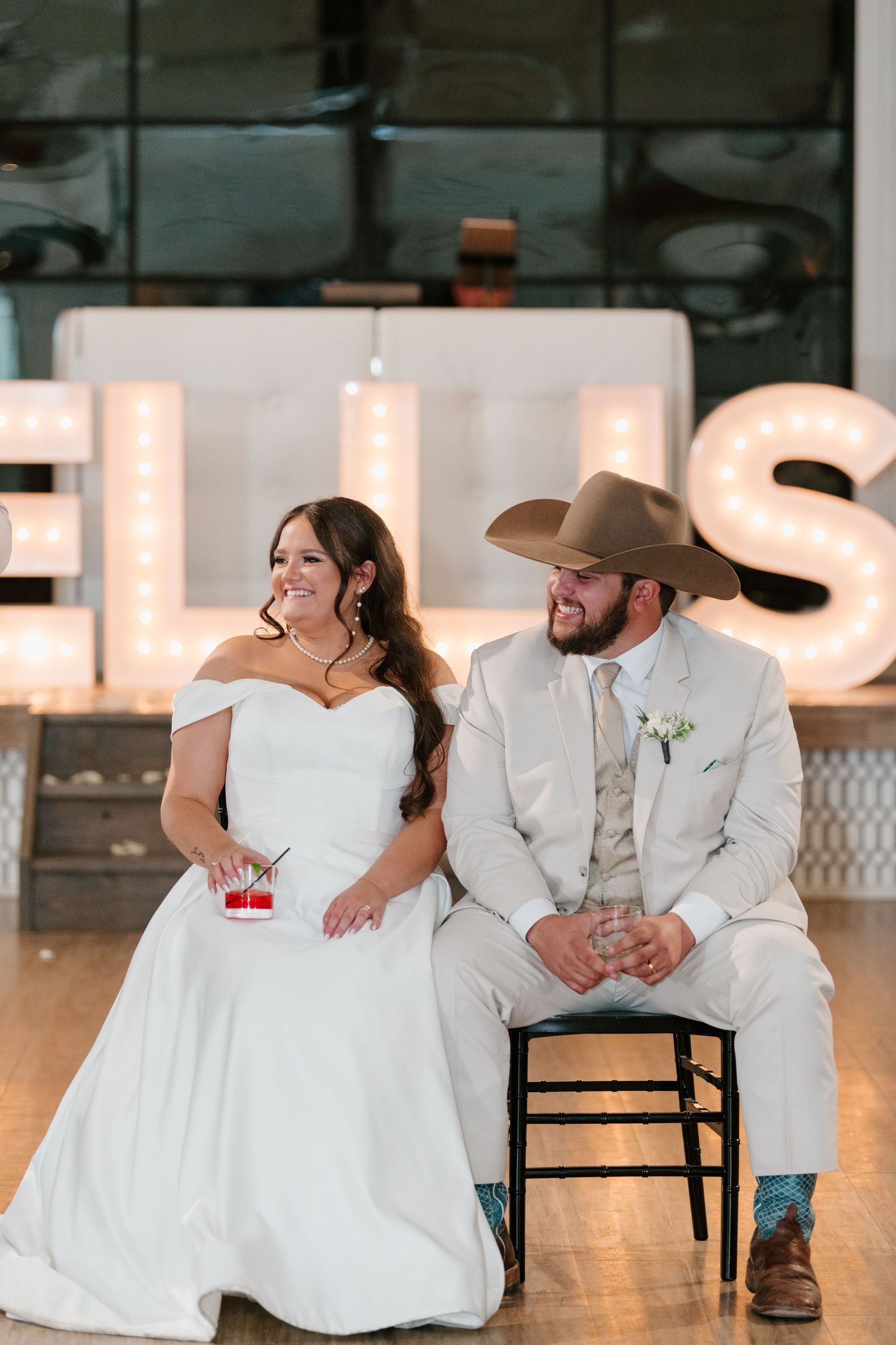 A couple sits together at their rustic themed wedding reception with illuminated letter decorations in the background.