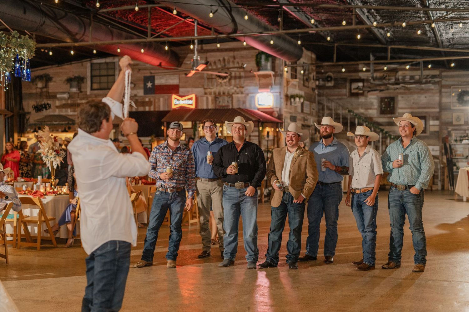 Line dance formation at rustic barn wedding reception with wooden walls and string lights.
