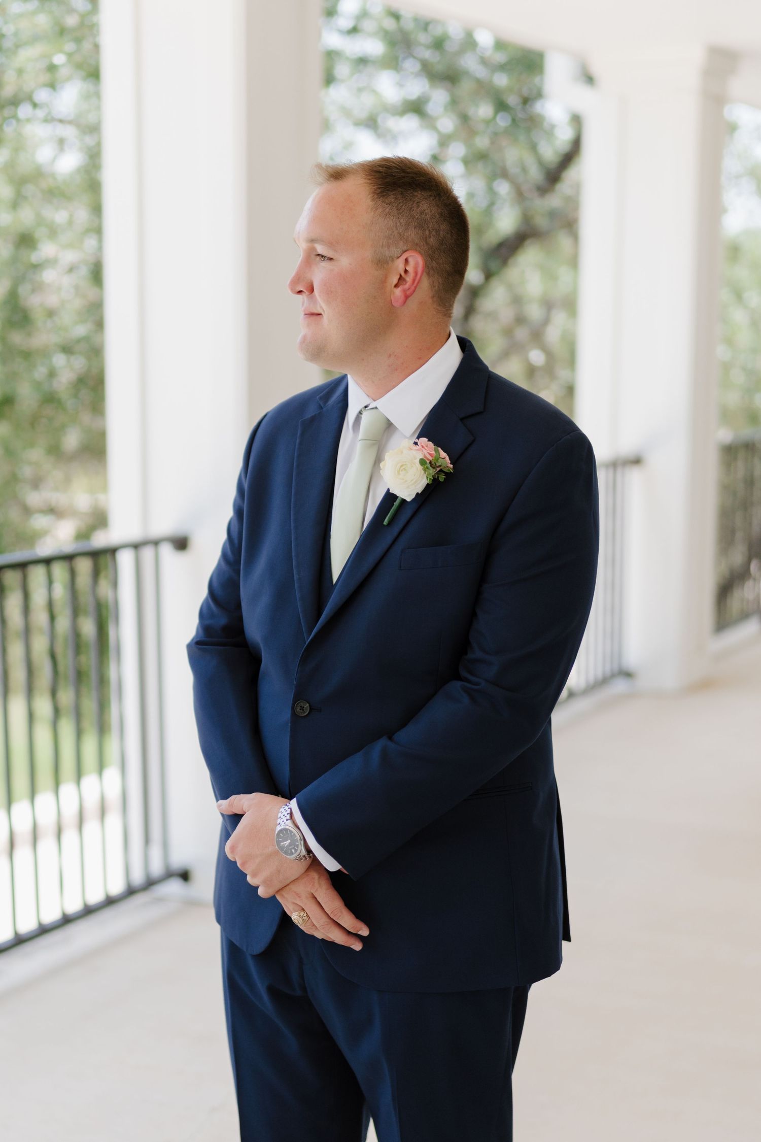 Groom in navy suit waiting on white columned porch before ceremony.