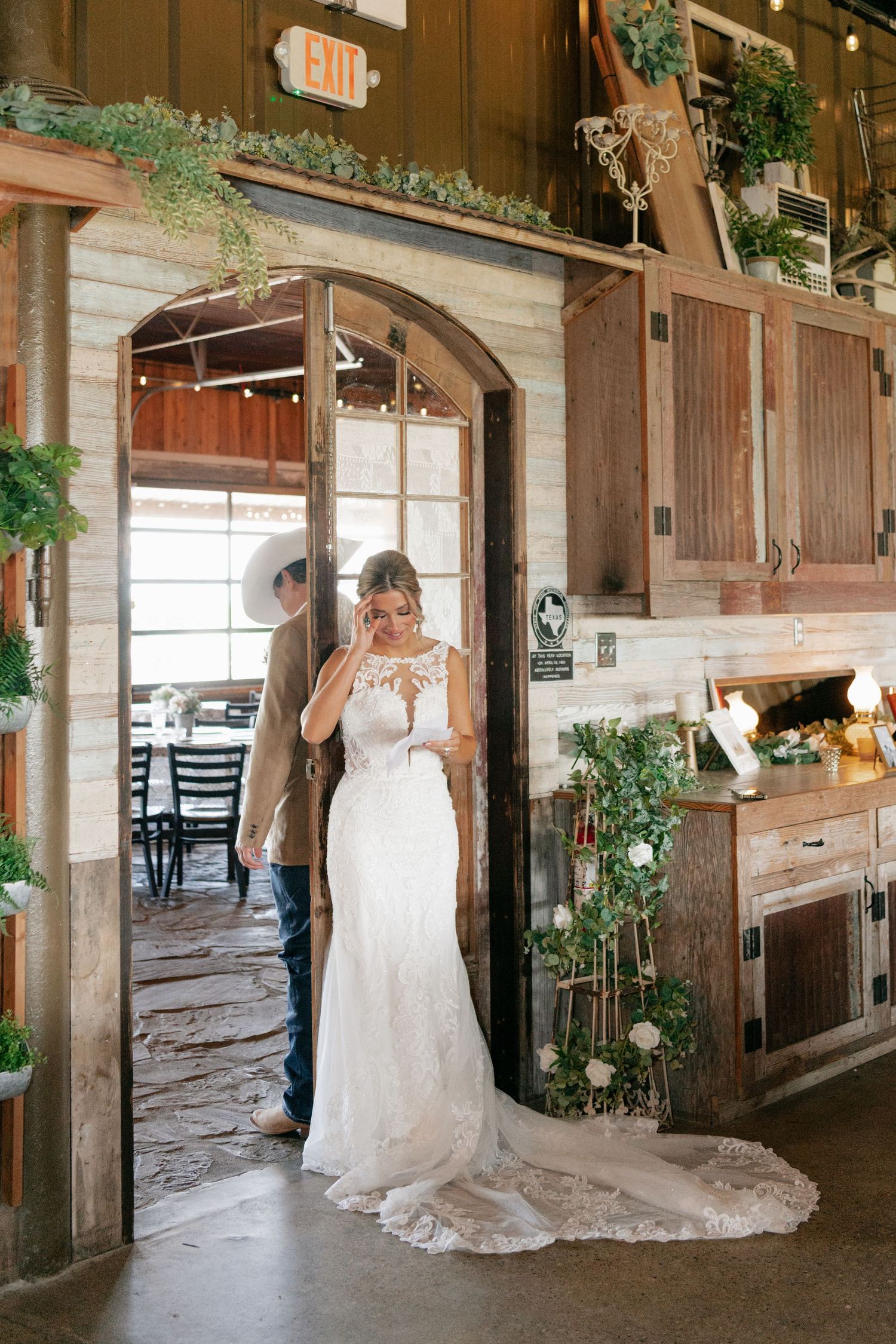 Elegant lace wedding dress with a flowing train photographed in a rustic barn venue with wooden details and greenery.