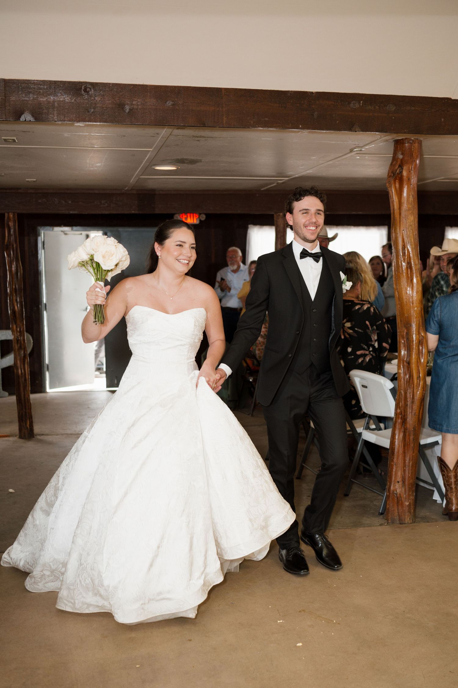 Newlyweds joyfully walk back down aisle after wedding ceremony, bride holding white bouquet.