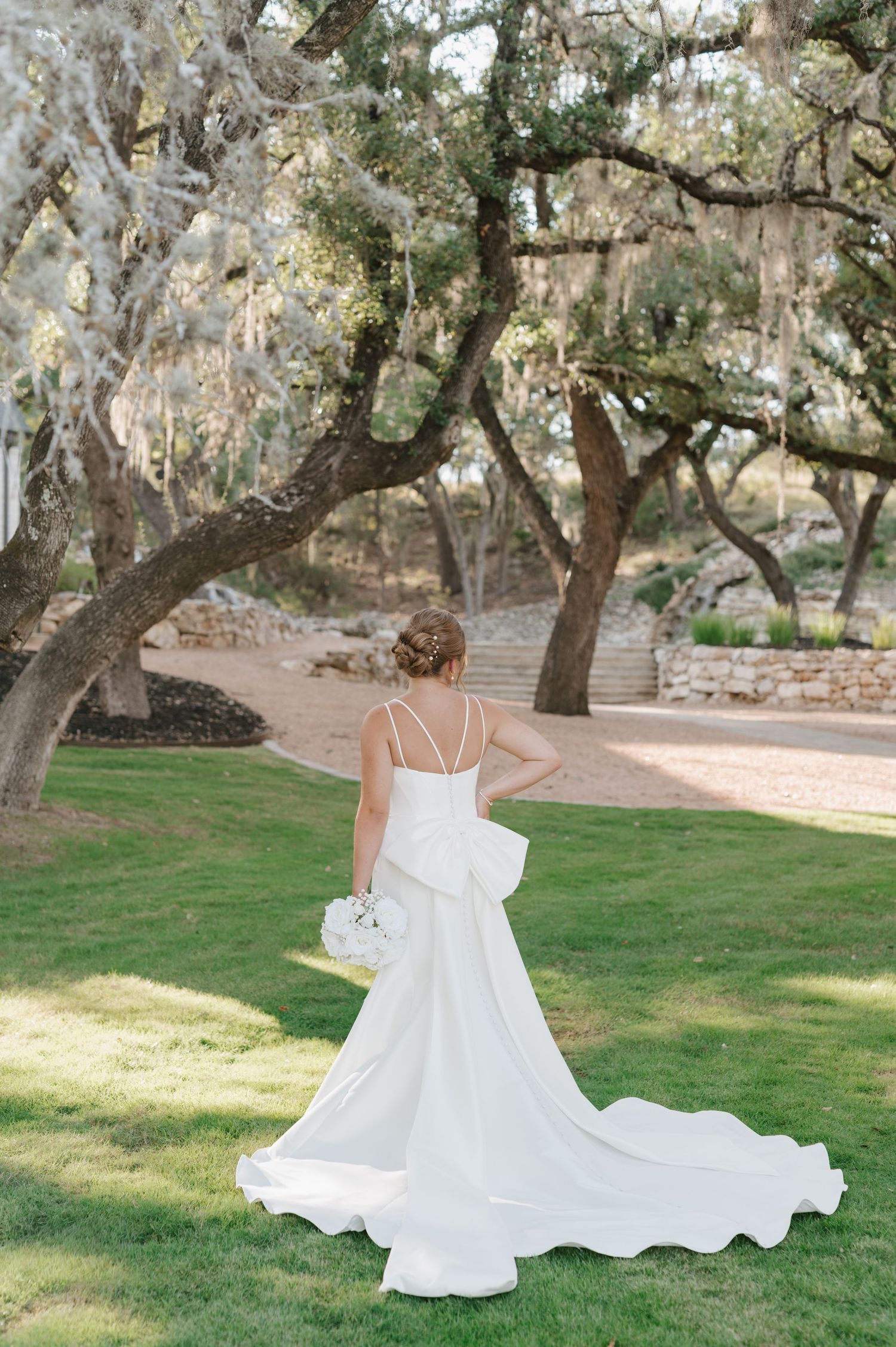 A flowing white dress twirls gracefully in a series of photos taken in a serene garden setting with oak trees.