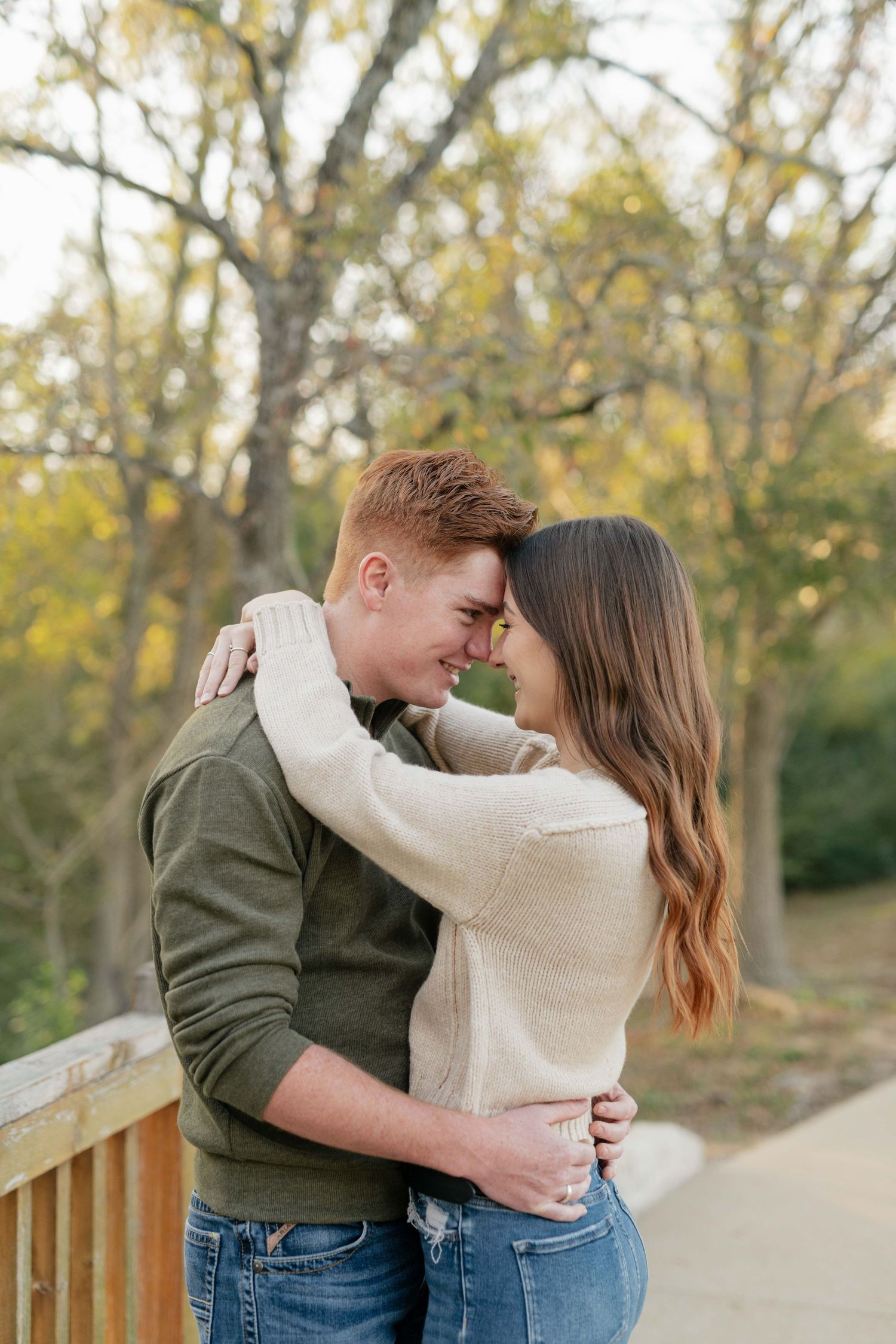 Intimate moment between a couple embracing on a wooden bridge surrounded by autumn trees.