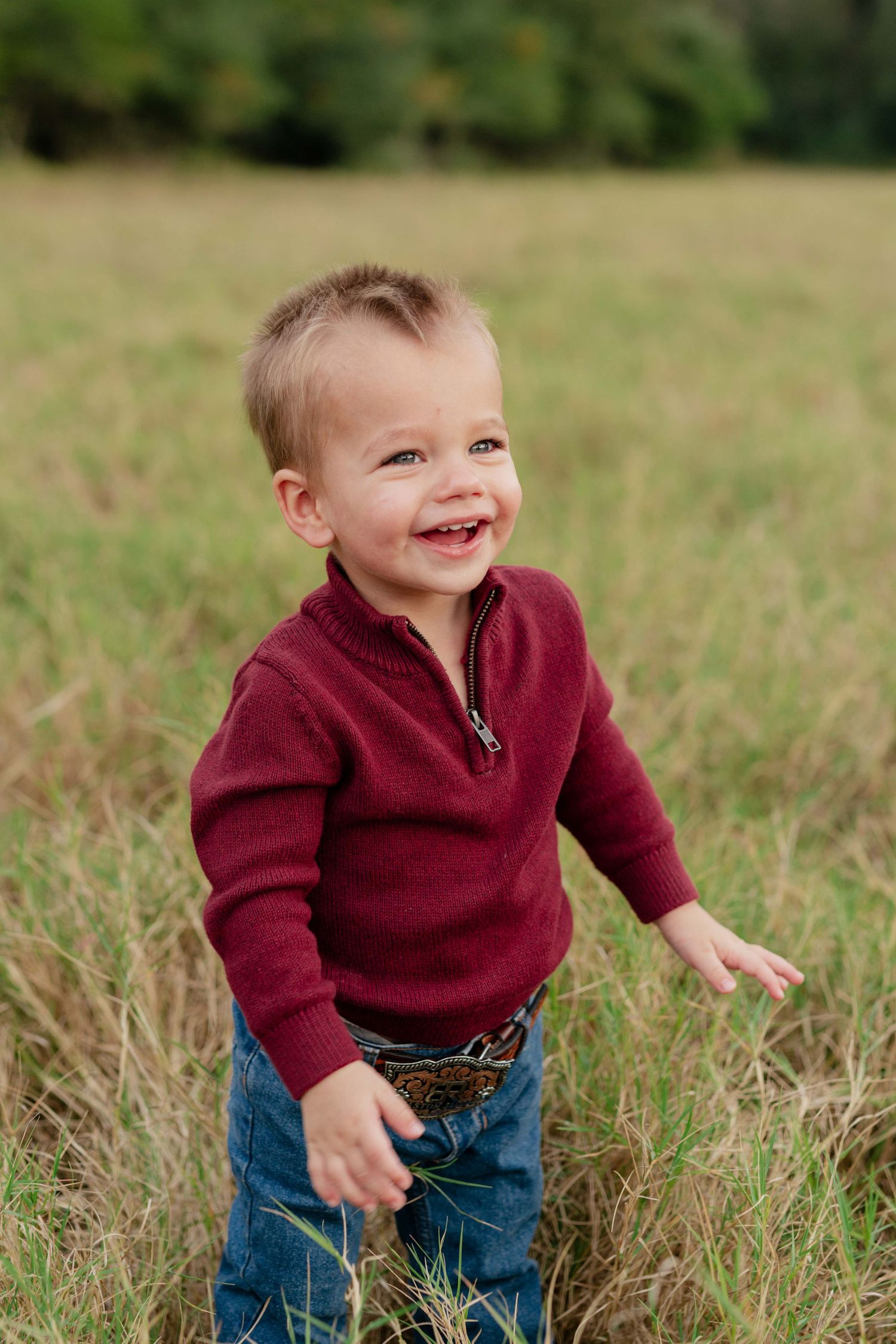 Young child in red sweater laughing while playing in a grassy field.