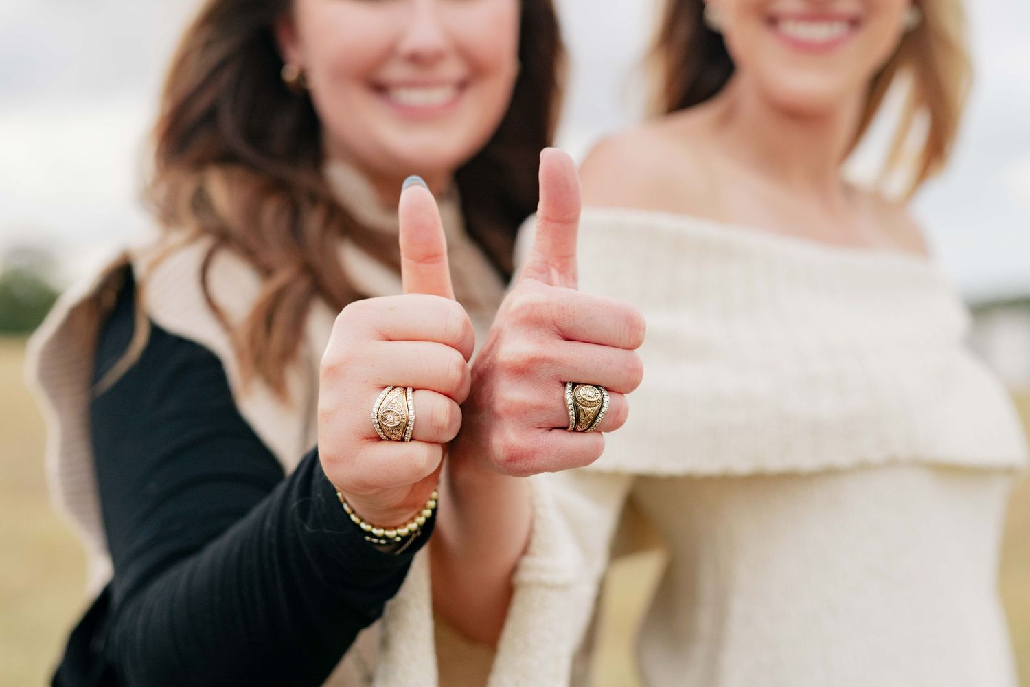 Close-up of hands showing off rings while giving thumbs up gestures outdoors.