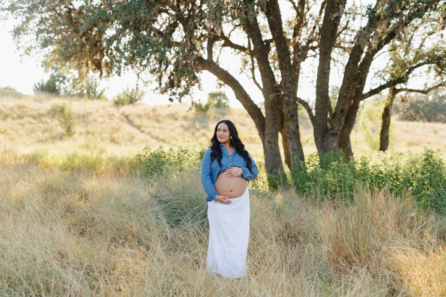 A couple shares an intimate moment in golden sunlight beneath oak trees in a rustic outdoor setting.