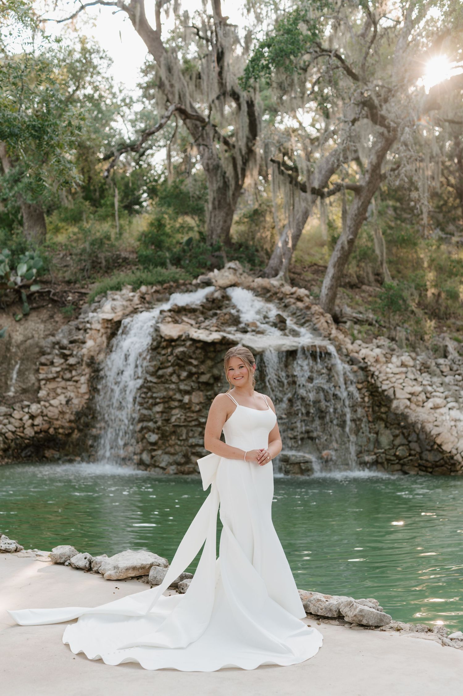 A stunning bridal portrait session by a waterfall and turquoise pool surrounded by natural stone.