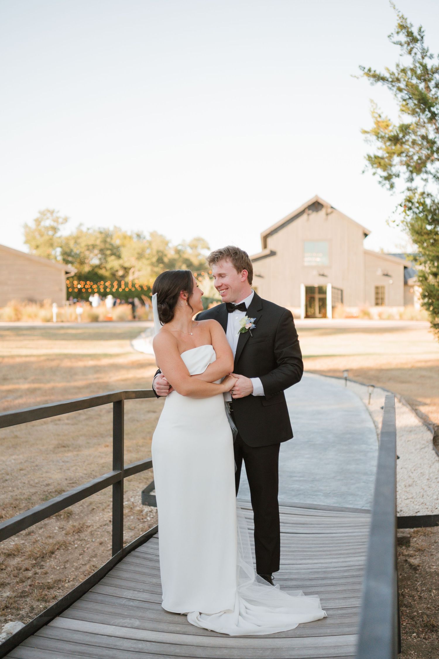 A couple in wedding attire shares a tender moment while sitting on a wooden boardwalk at sunset.