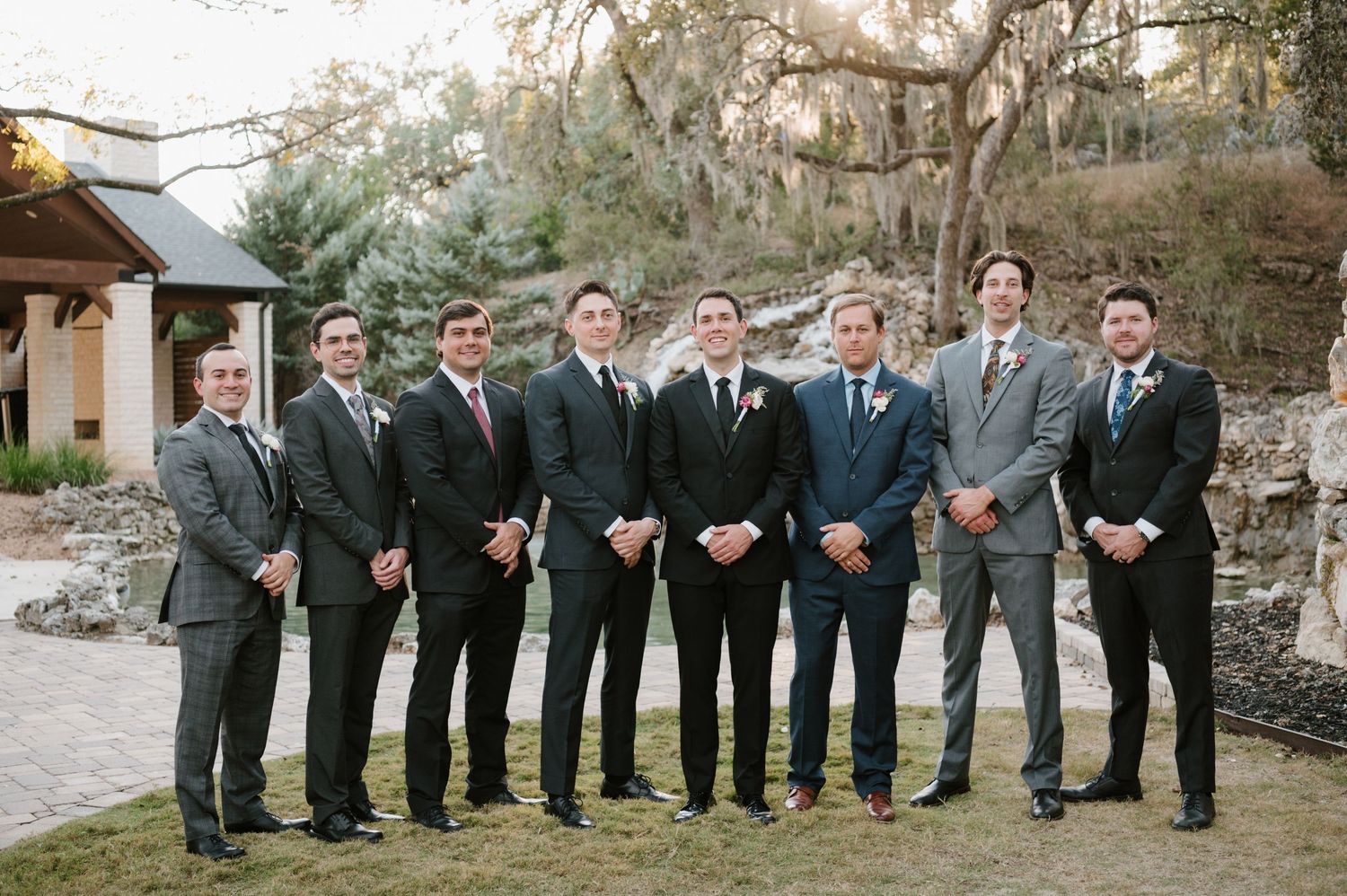 Wedding party members in formal attire standing in a line outdoors.