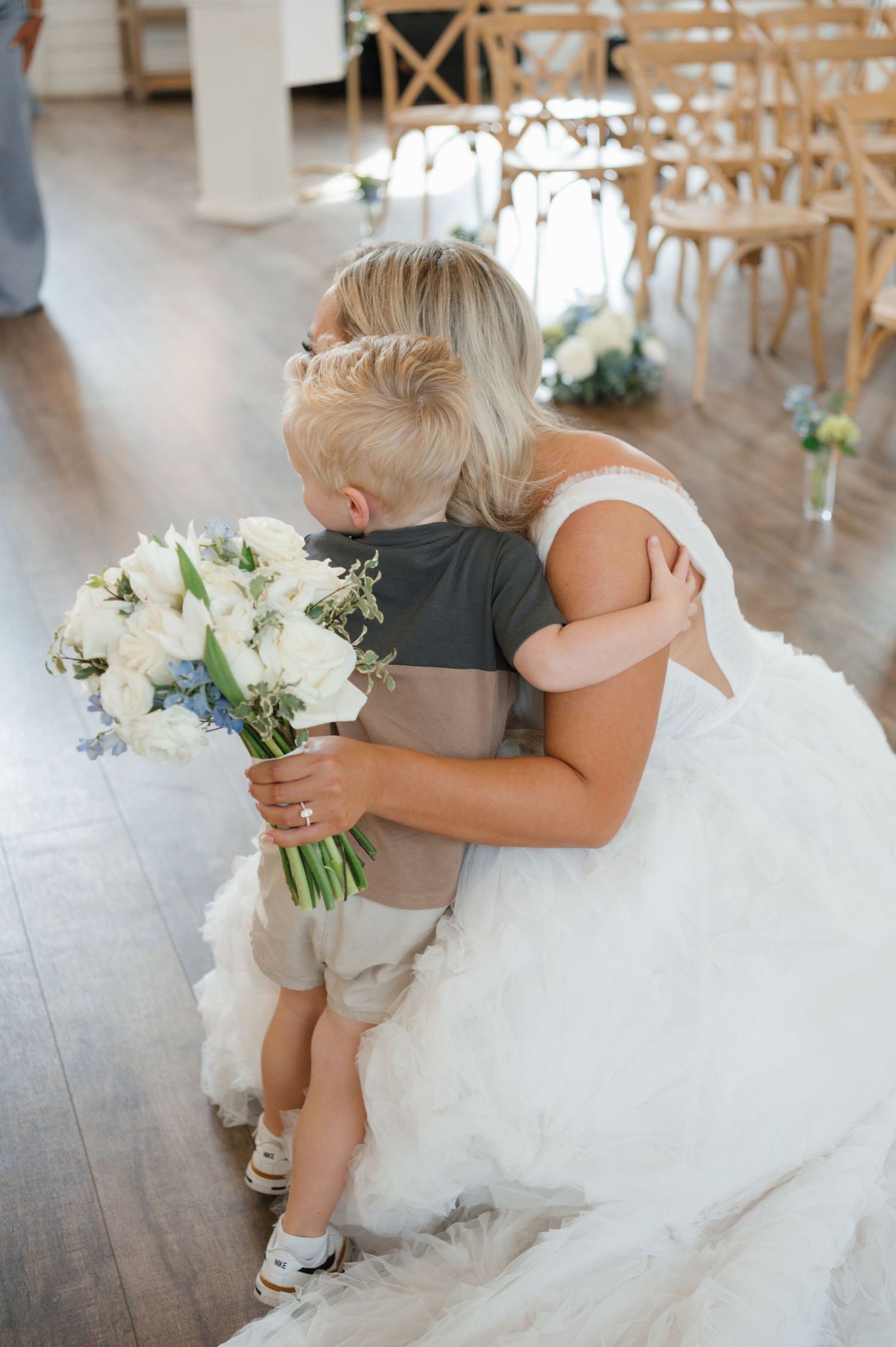 A bride holding a bouquet of flowers and embracing a young child.