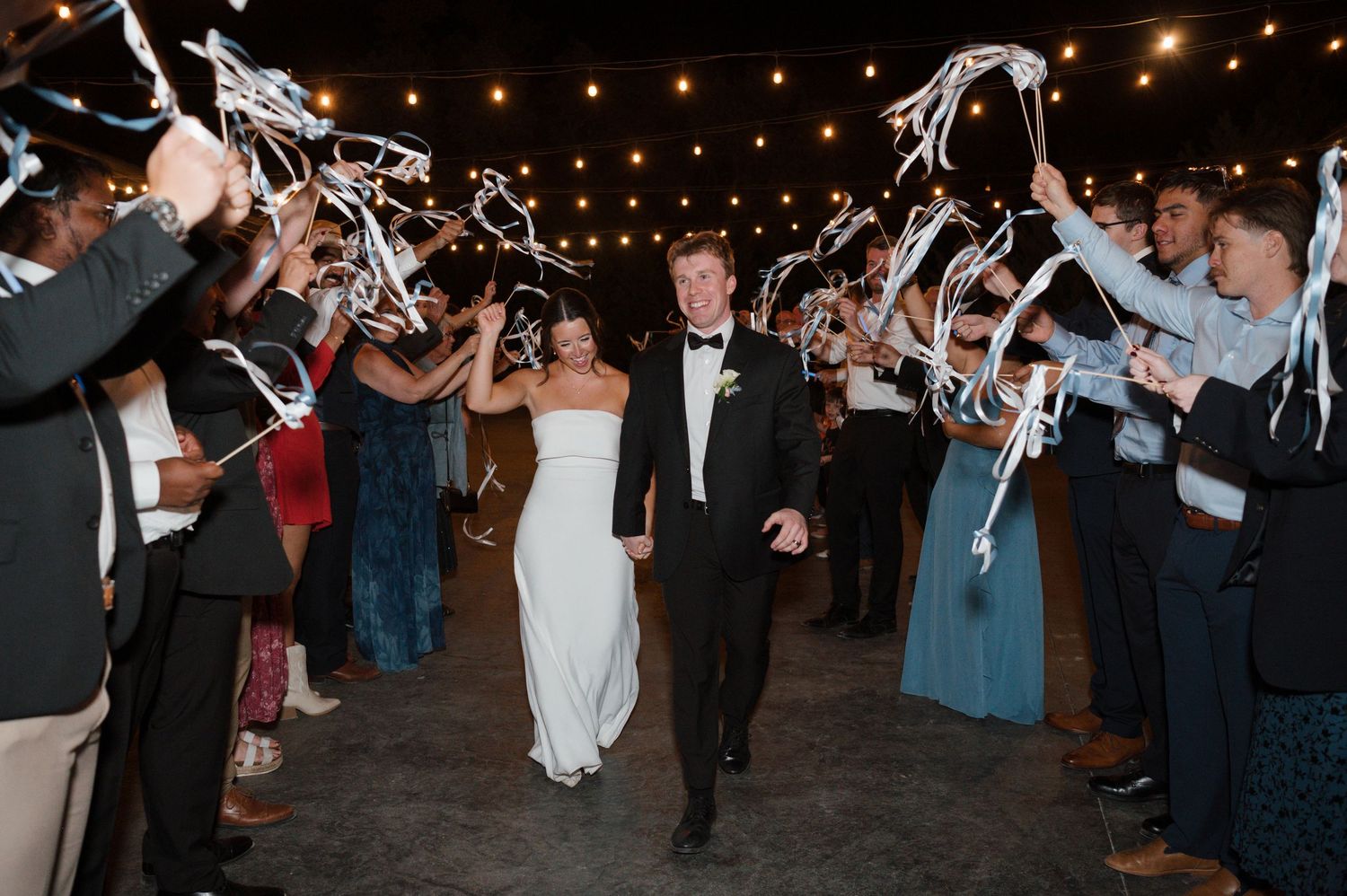A couple walks through a tunnel of guests holding sparklers during an evening wedding celebration.