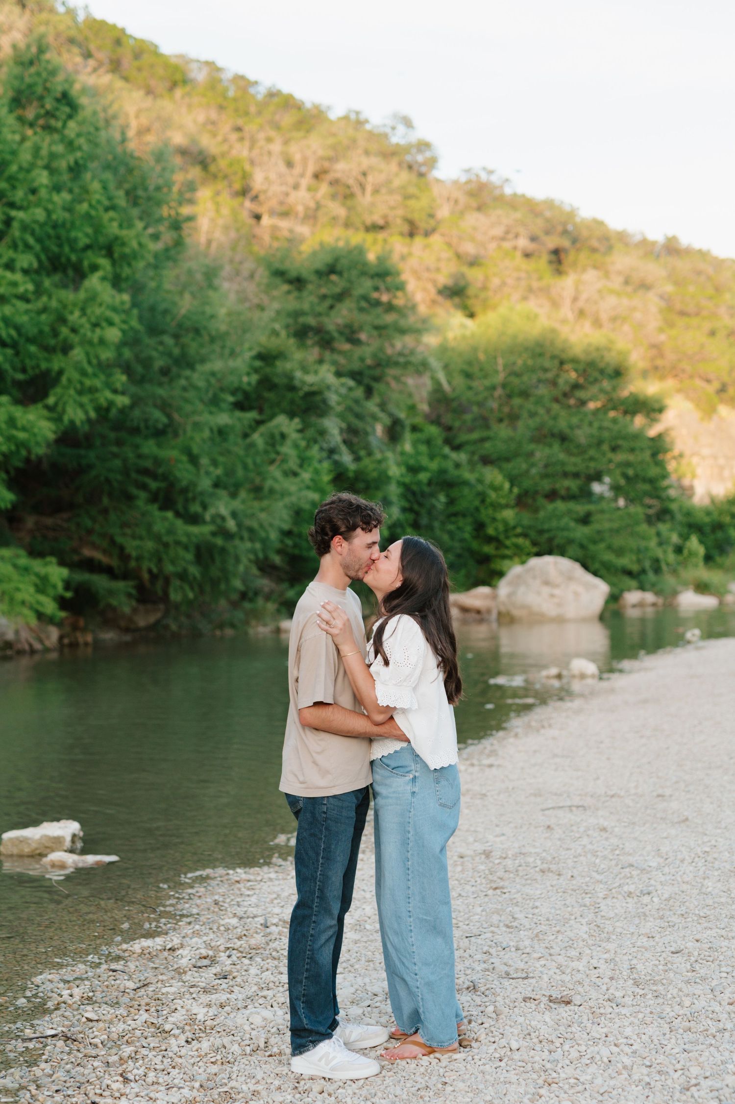 Intimate couple portraits on rocky riverbank with sunlit hills in the background.
