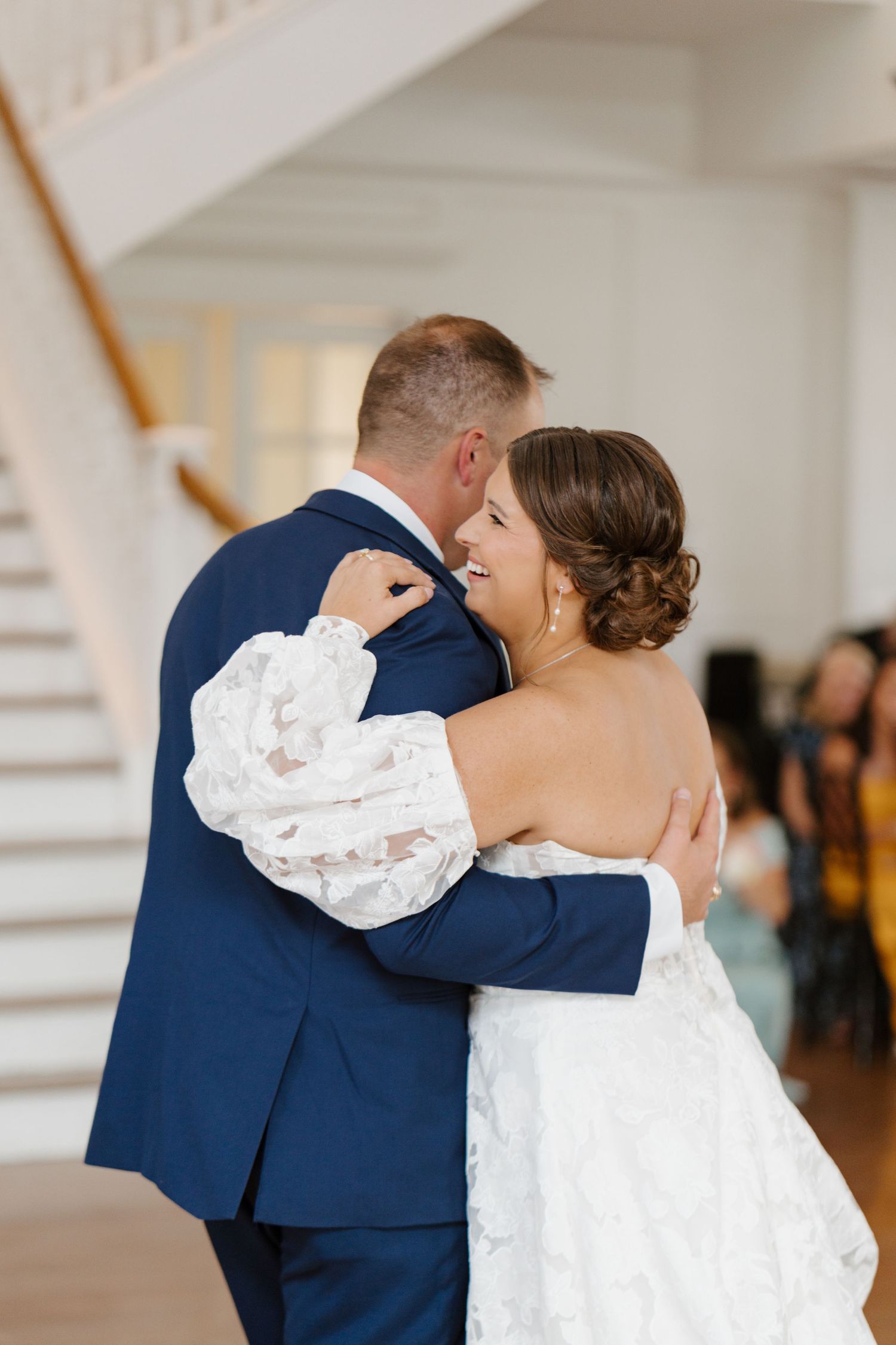 Bride in white wedding gown and groom in navy suit share a romantic dance at their reception.