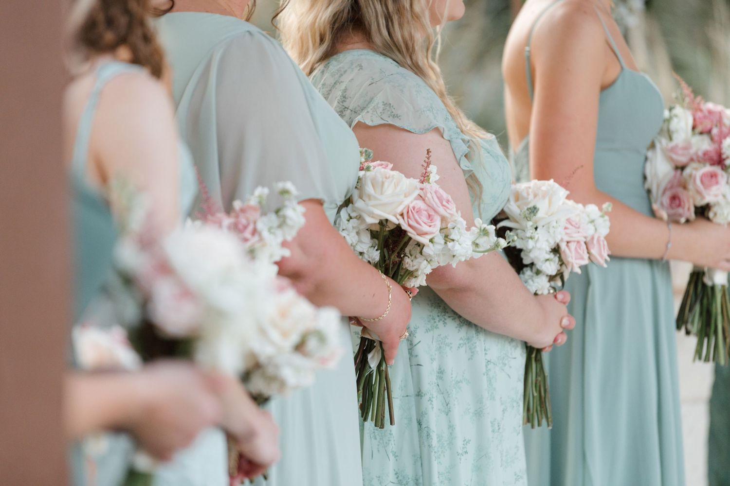 Bridesmaids in soft blue dresses holding pink bouquets stand in a row.