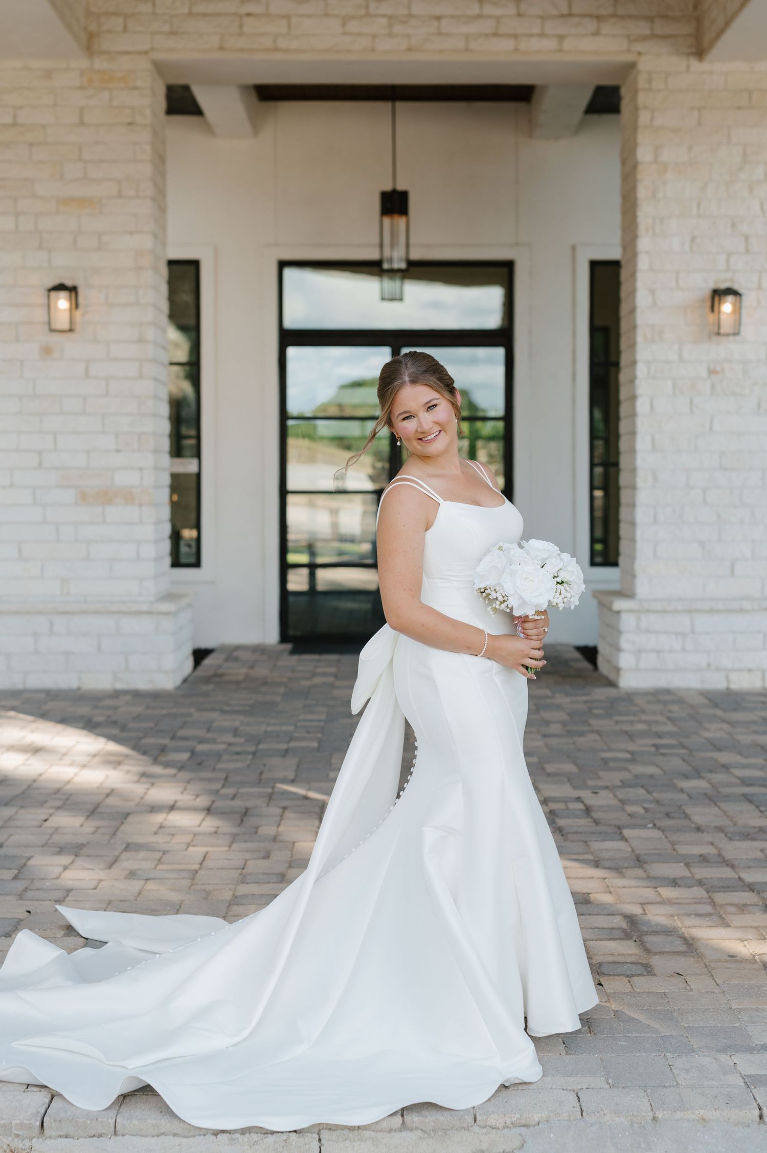 Elegant bride in a flowing white gown twirls on a stone patio in front of a light brick building.