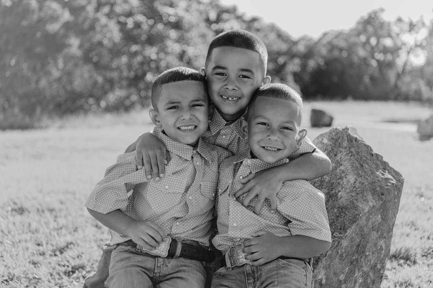 Three young children sitting together and smiling outdoors in a black and white vintage photograph.