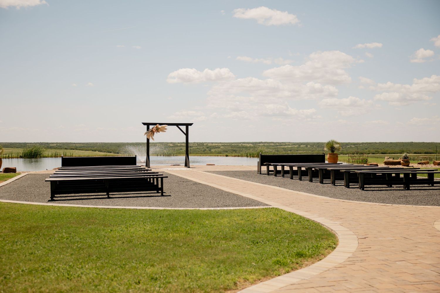 Outdoor wedding ceremony setup with wooden arch and benches on concrete platform against vast prairie landscape.