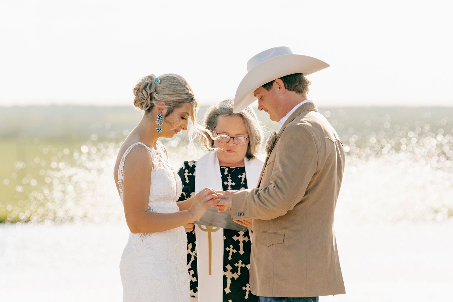 A couple exchanges vows during an outdoor beach wedding ceremony with an officiant on a sunny day.
