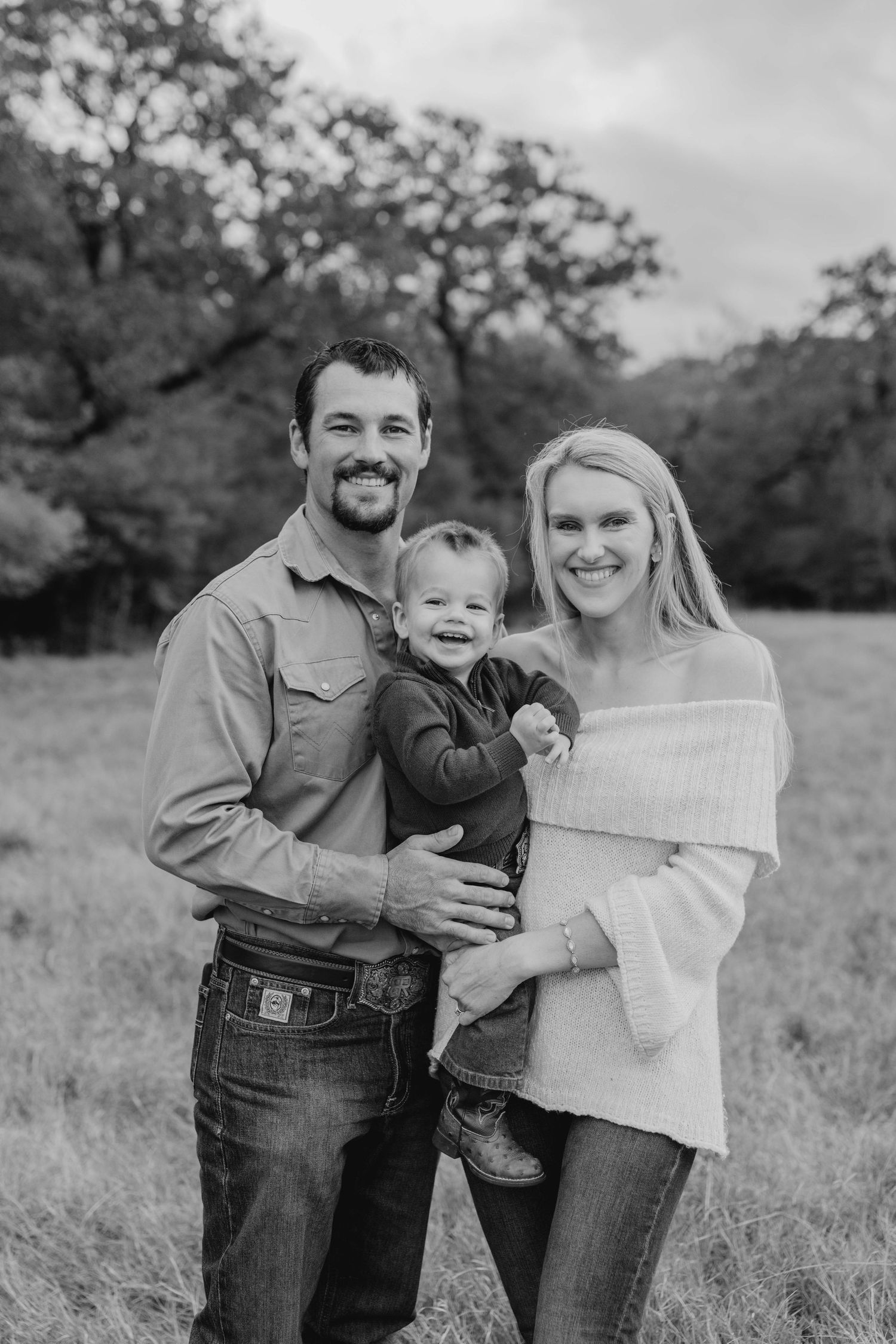 A family poses together in a grassy field with trees in the background.