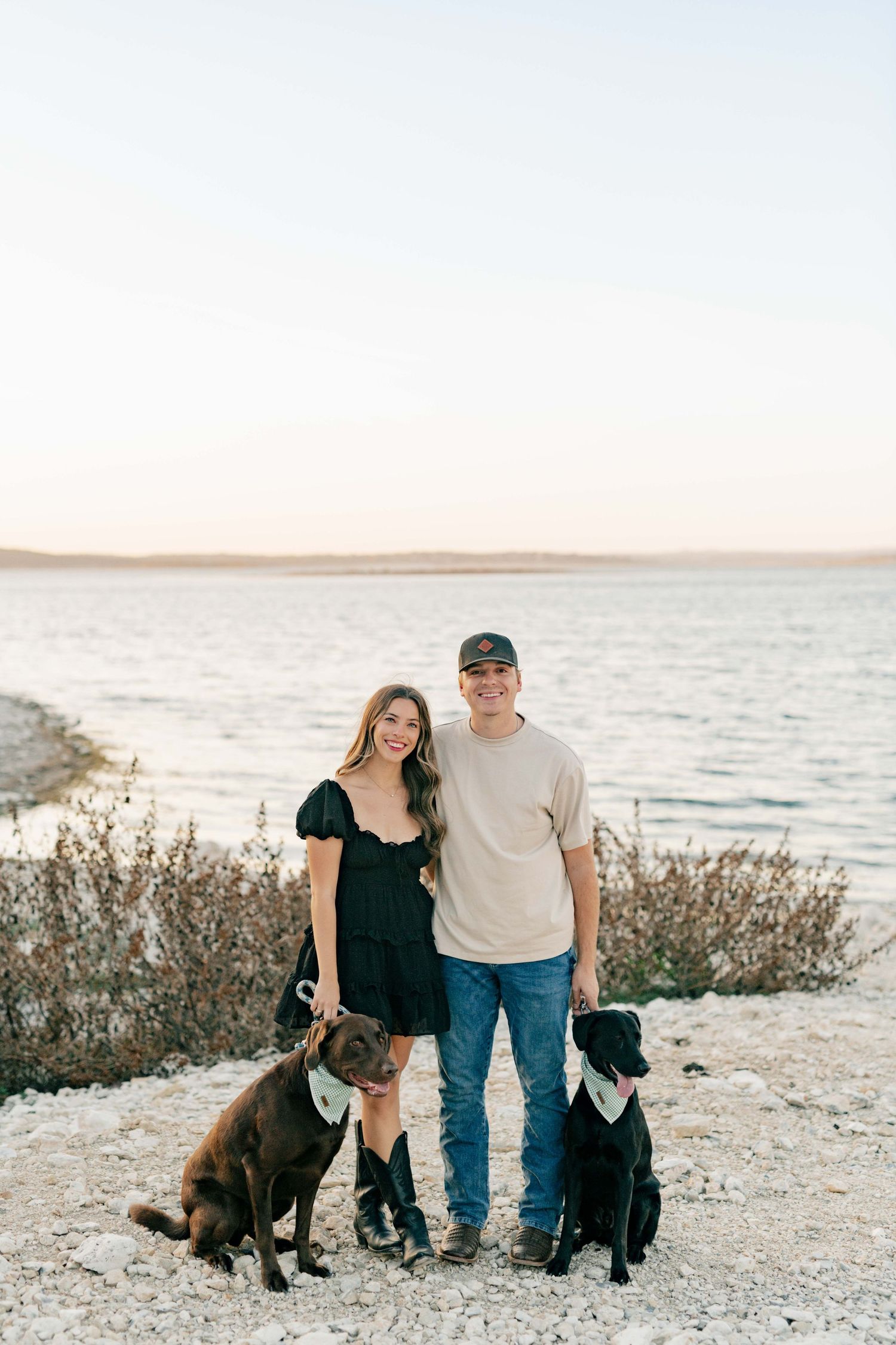 Couple poses with their two dogs on a lakeside cliff during a beautiful evening.