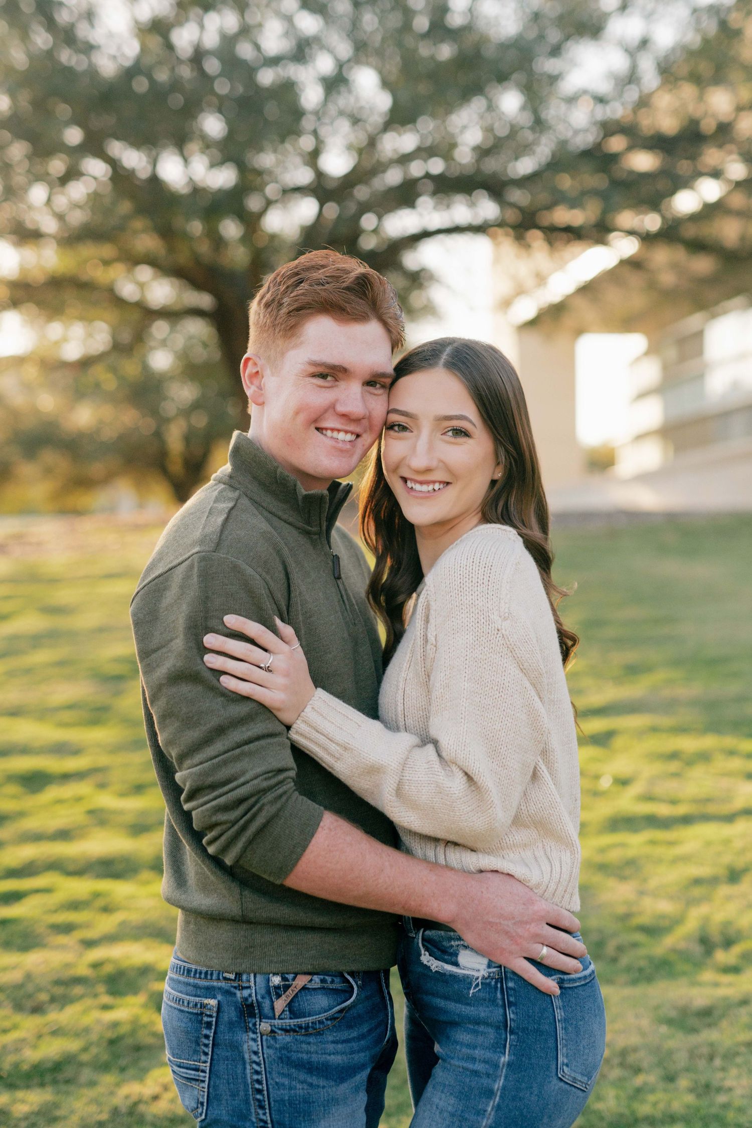 A couple in matching sweaters embraces while smiling outdoors.