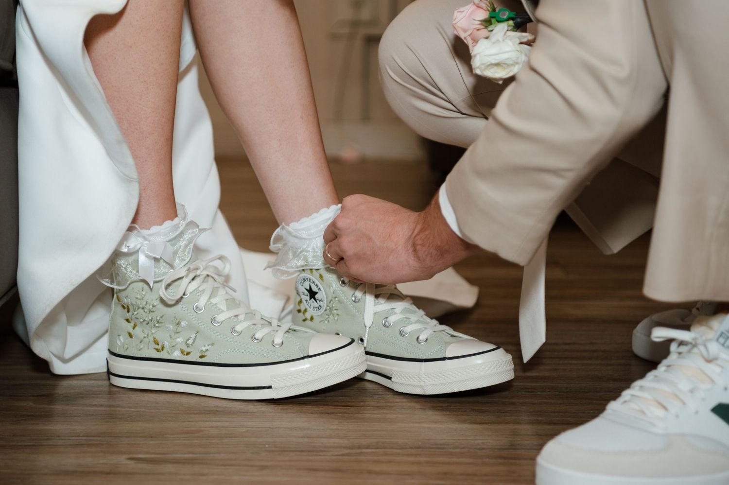 A close-up view of white lace Converse sneakers worn with a wedding dress at a wedding ceremony.