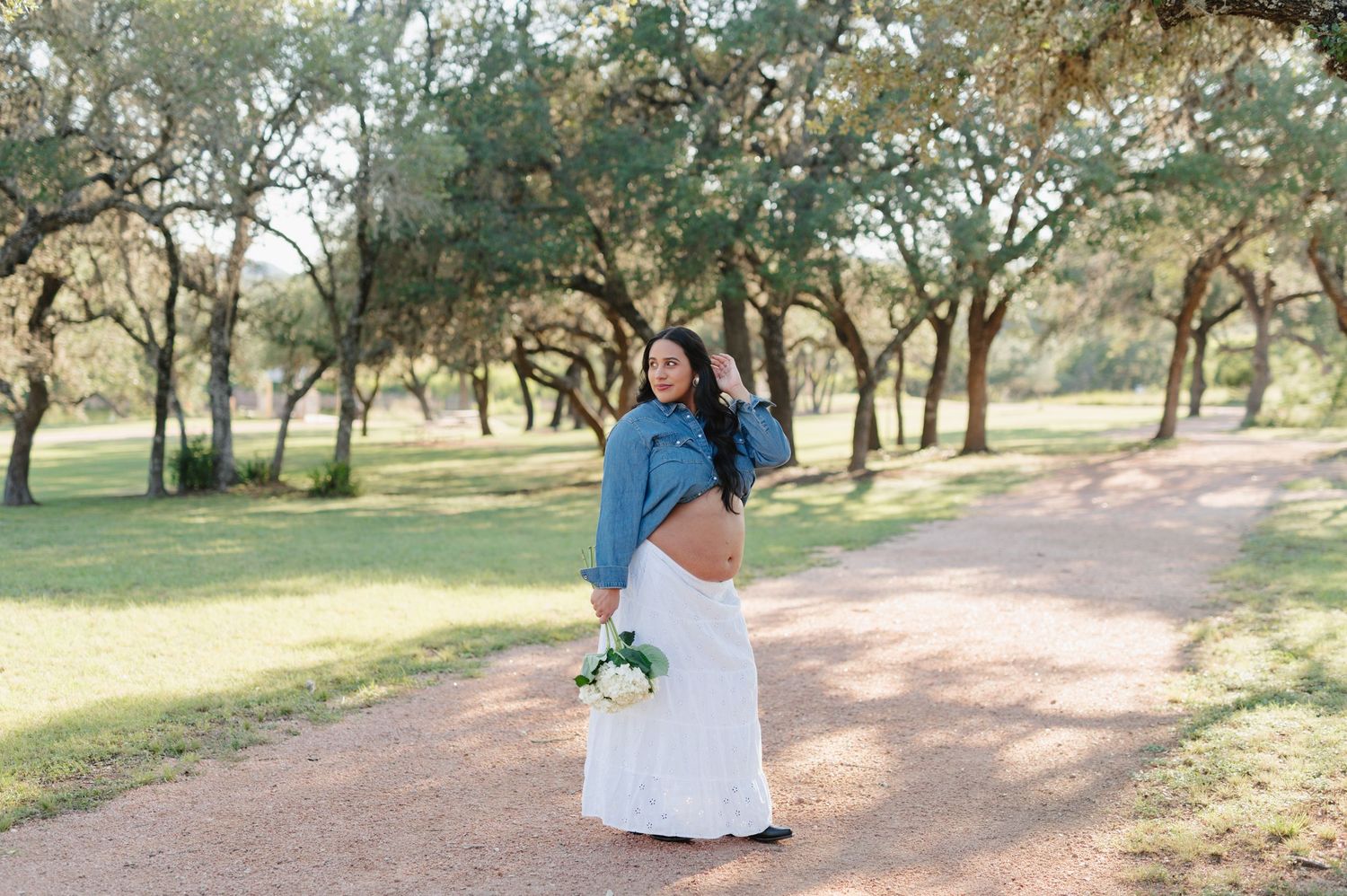 A pregnancy announcement photoshoot captured on a scenic trail with oak trees in the background.