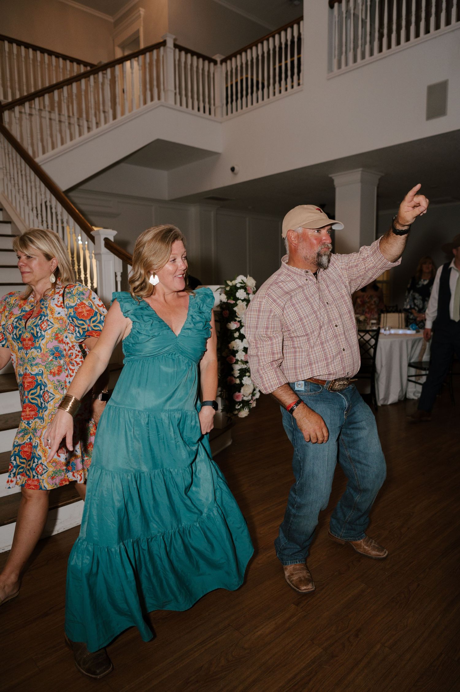 Line dancers in turquoise dresses performing a coordinated dance routine on a wooden floor.