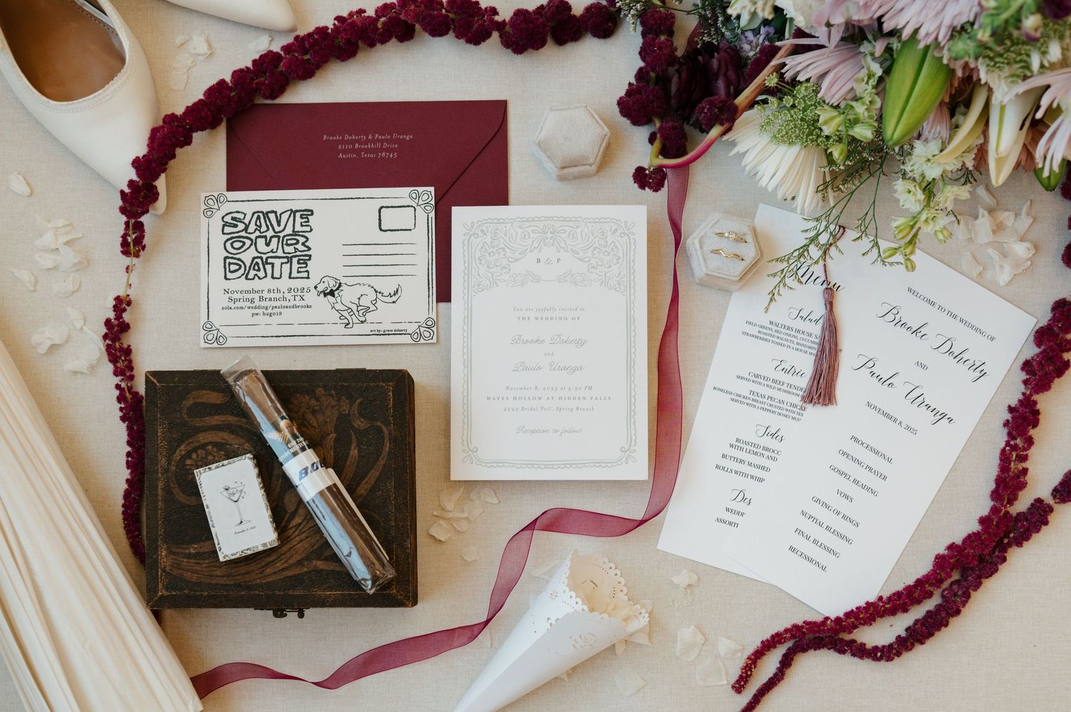 Wedding stationery flatlay with burgundy amaranthus flowers and elegant white invitations on a neutral background.