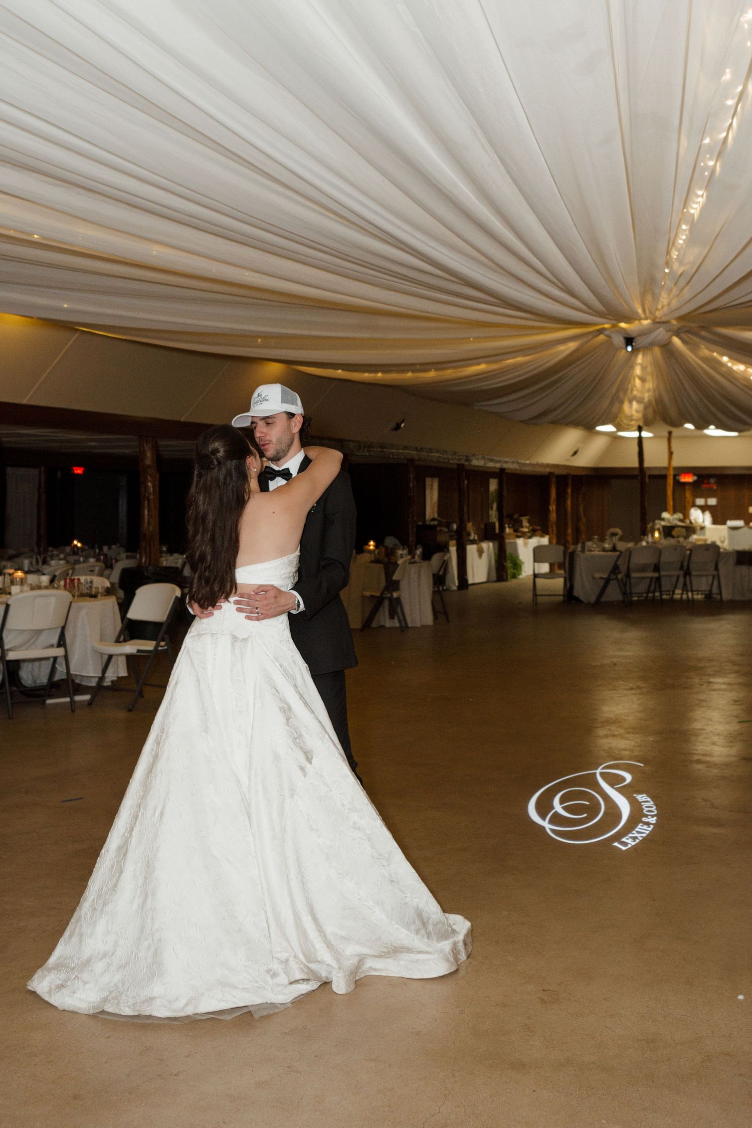 Bride and groom share their first dance in a elegantly draped wedding reception venue with warm ambient lighting.