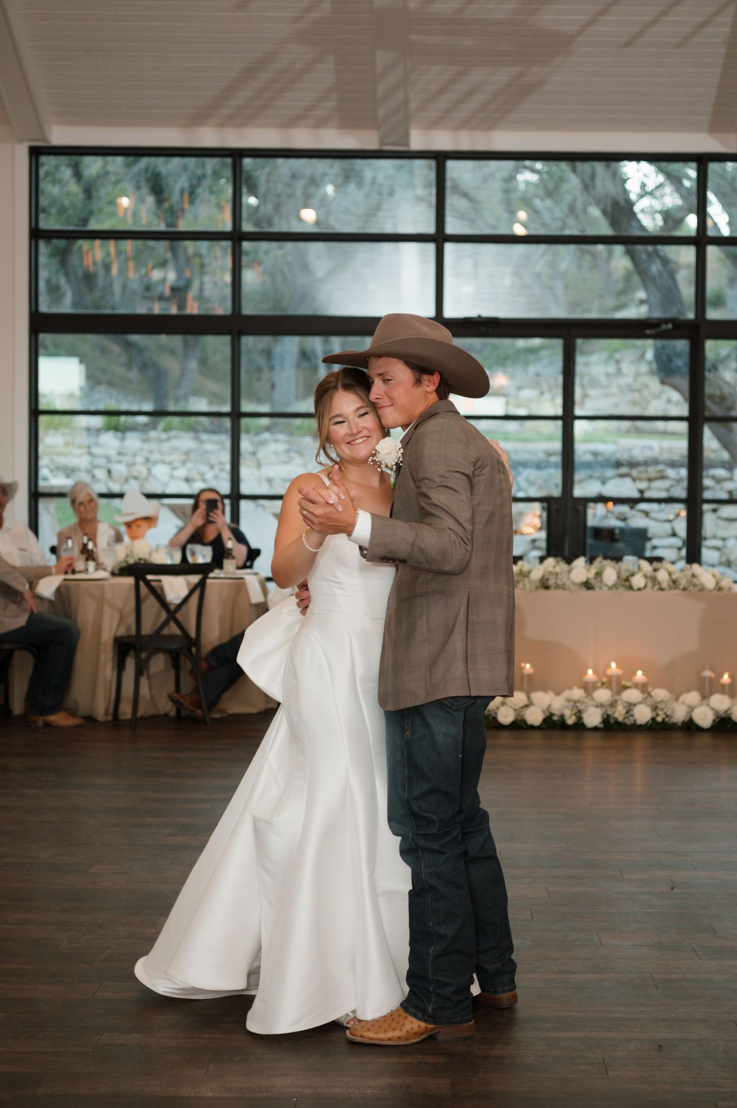 First dance in an elegant reception venue with large windows and floral decorations.