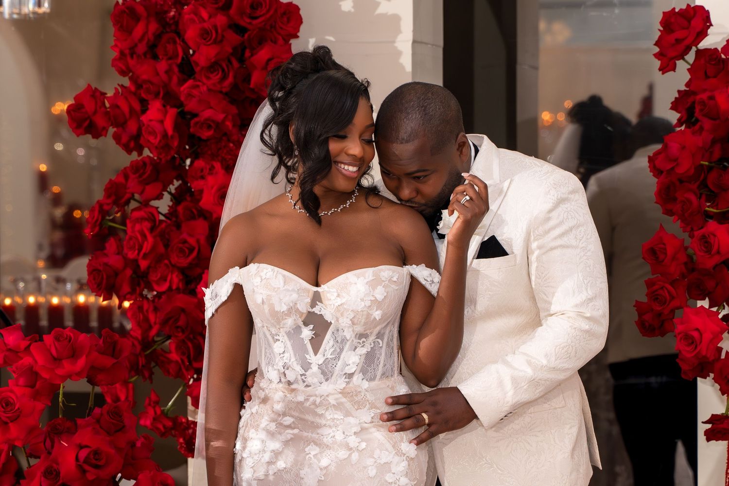 Wedding couple shares intimate moments against a backdrop of vibrant red floral arrangements at an elegant venue.