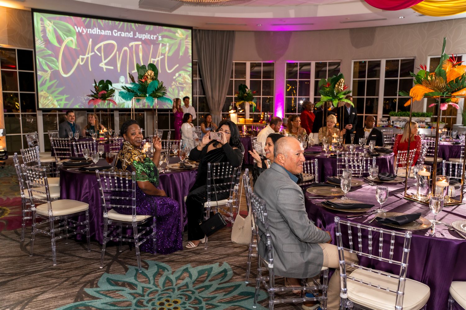 Elegant event space setup with purple tablecloths and decor featuring projected tropical graphics.