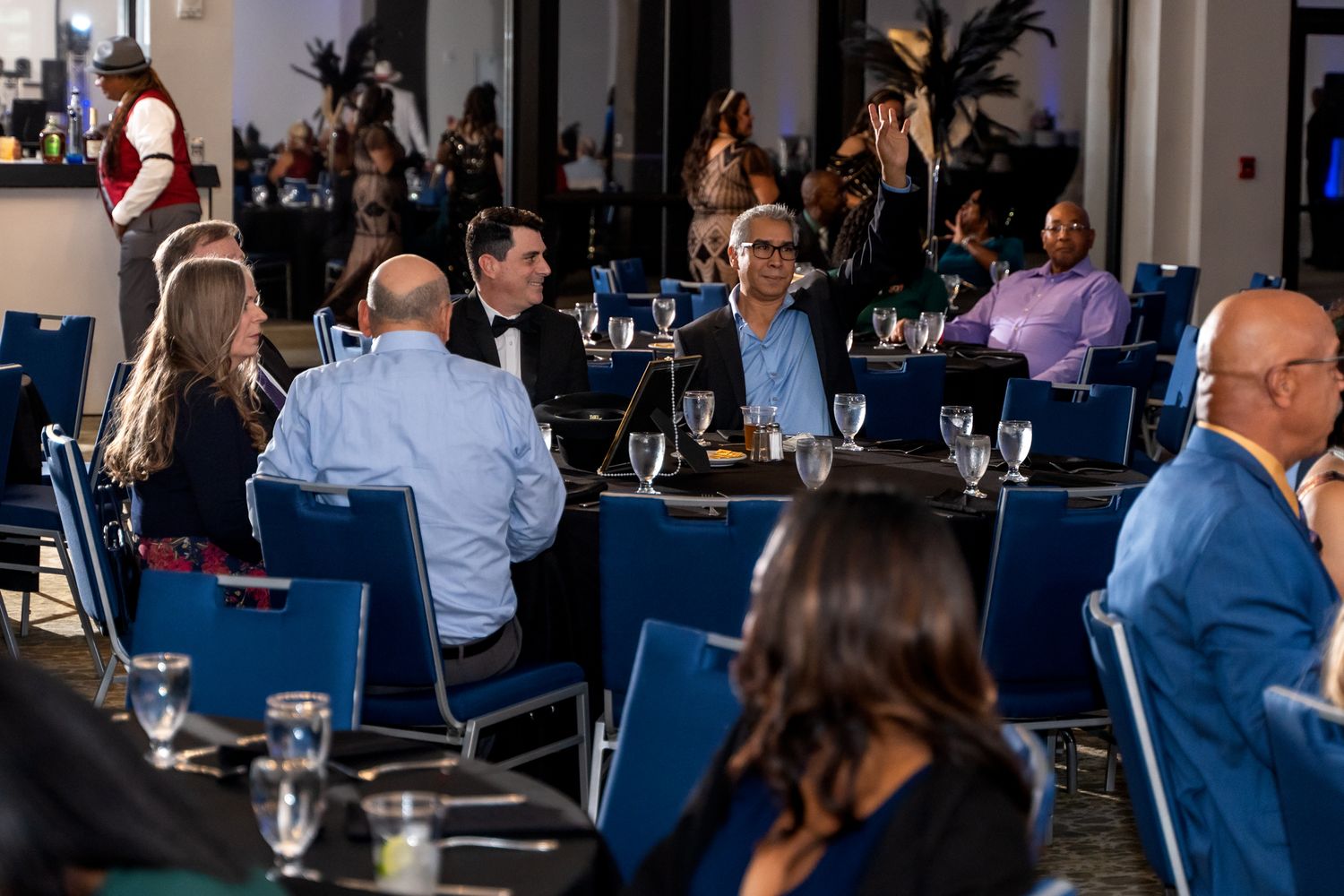 Guests seated at blue-decorated tables enjoy a formal dining event with feather centerpieces.