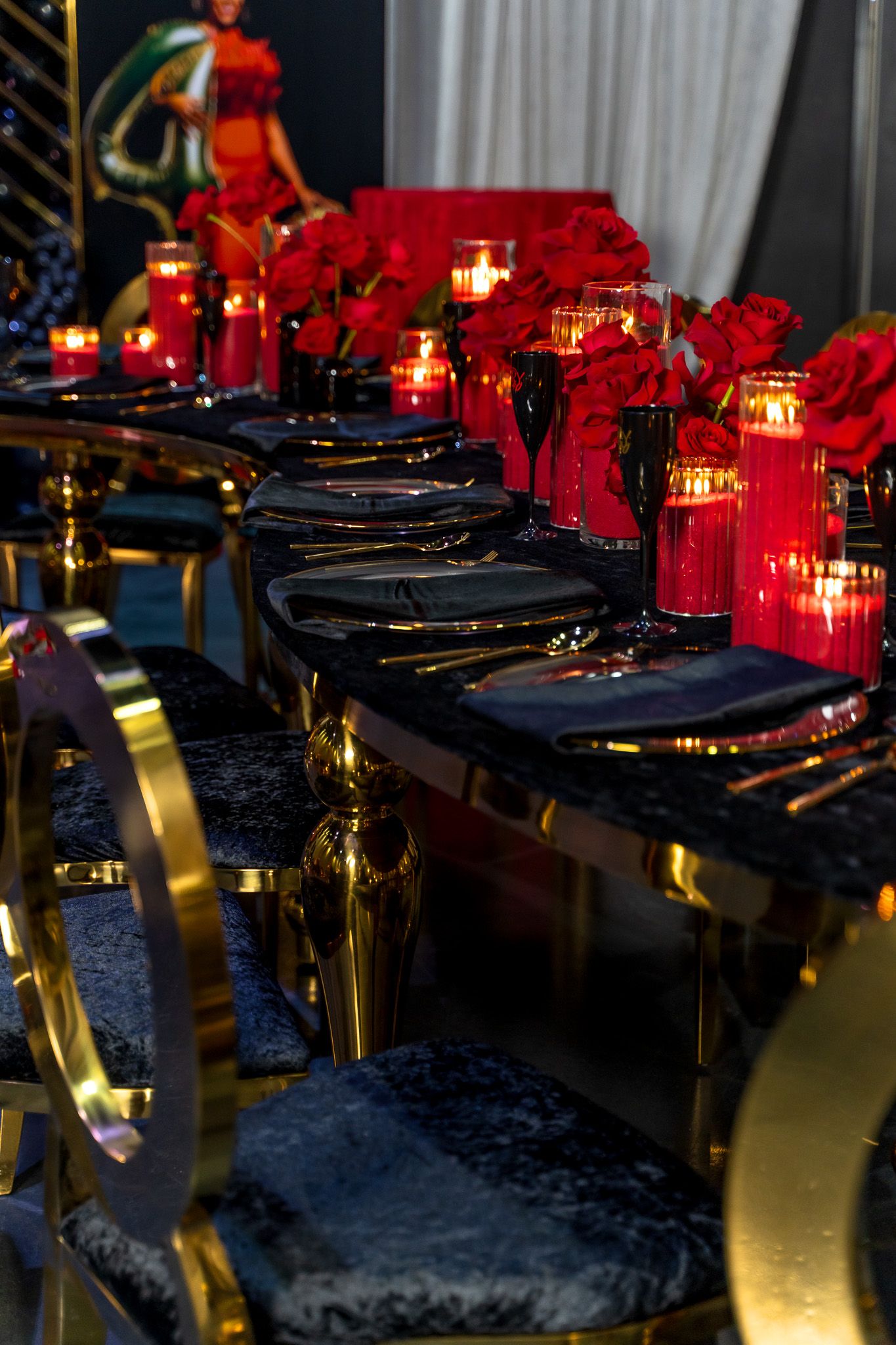 Elegant table setting with red roses, candles, and gold accents on dark velvet chairs.