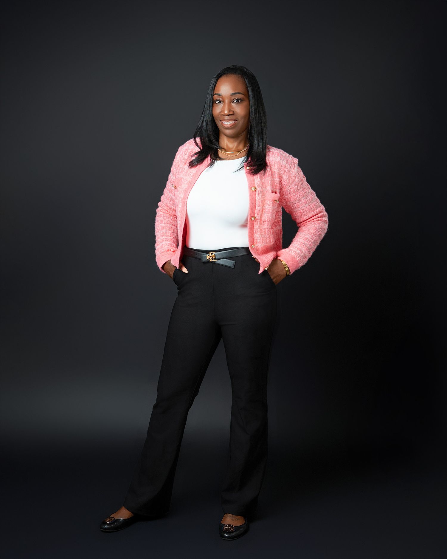 Professional portrait showing someone in a pink jacket with white top and black pants.